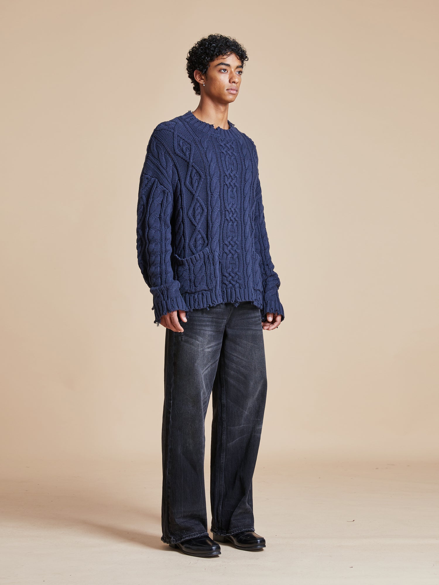 A man wearing the Found Astral Distressed Cable Knit Sweater in a blue color.