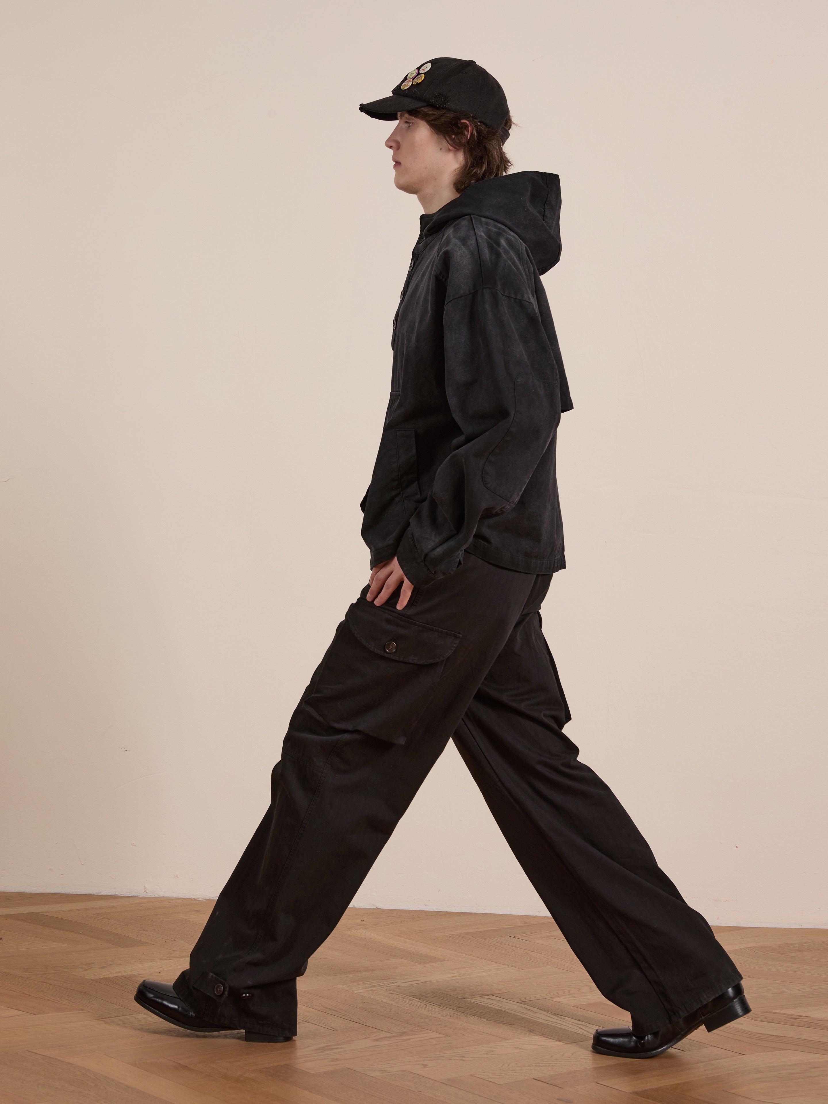 A person in a FOUND Washed Twill Pocket Anorak Jacket with a unisex relaxed fit casually strolls on a wood floor, their wide-leg pants swaying gently.