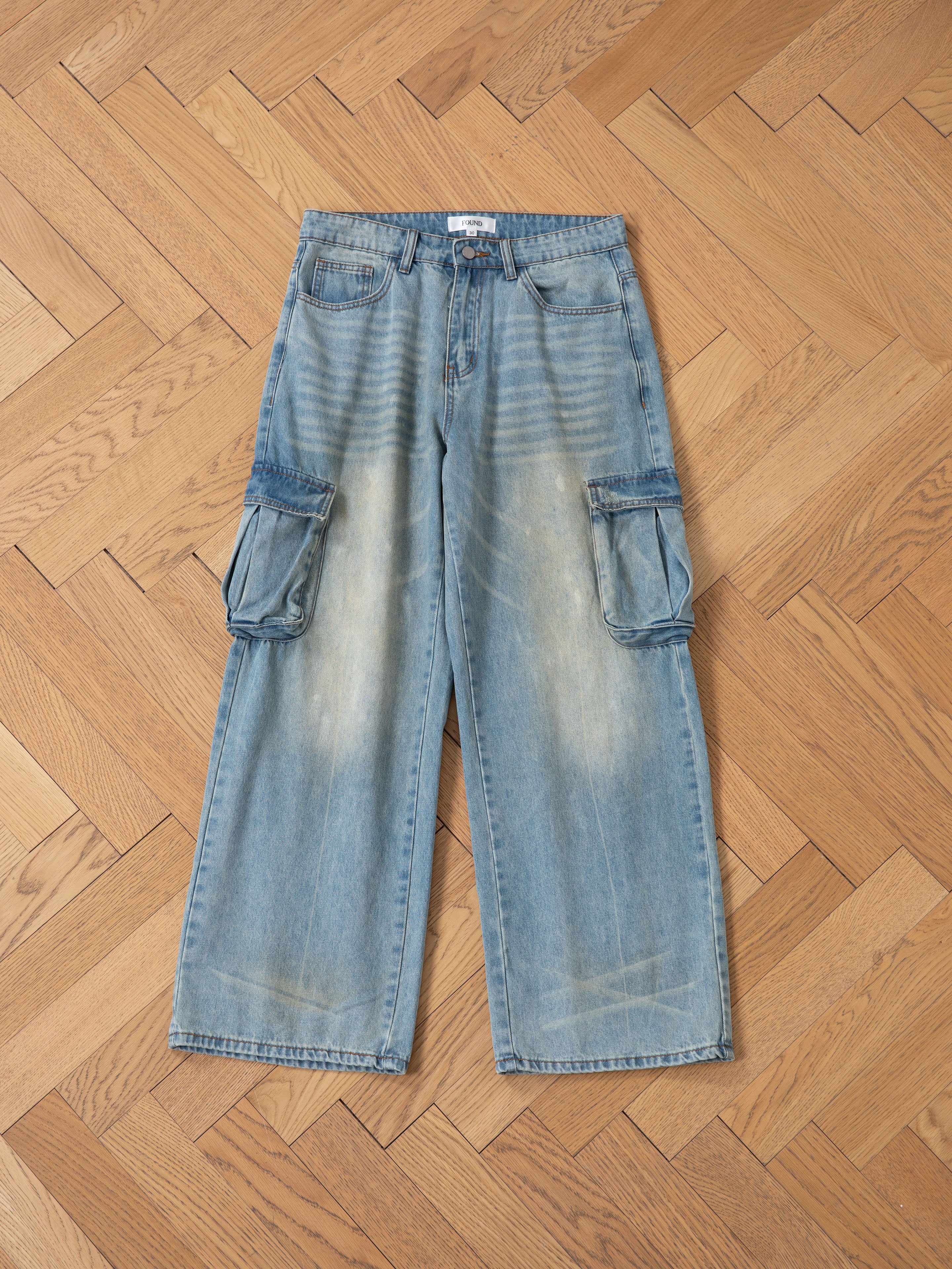 FOUND's wide-leg cargo jeans in blue, featuring a relaxed fit and utilitarian edge, are displayed flat on a wooden herringbone floor.