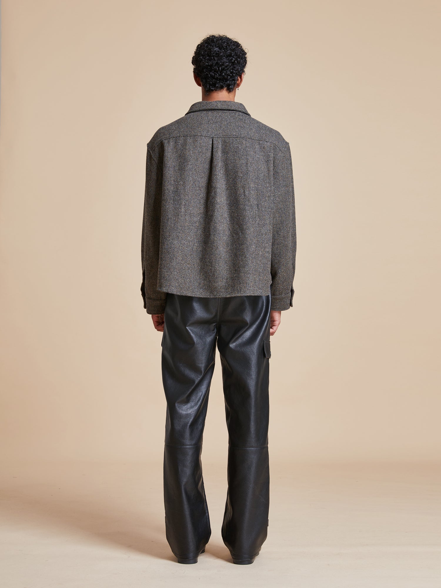 The back view of a man wearing a Found Raven Herringbone Overshirt and leather pants.