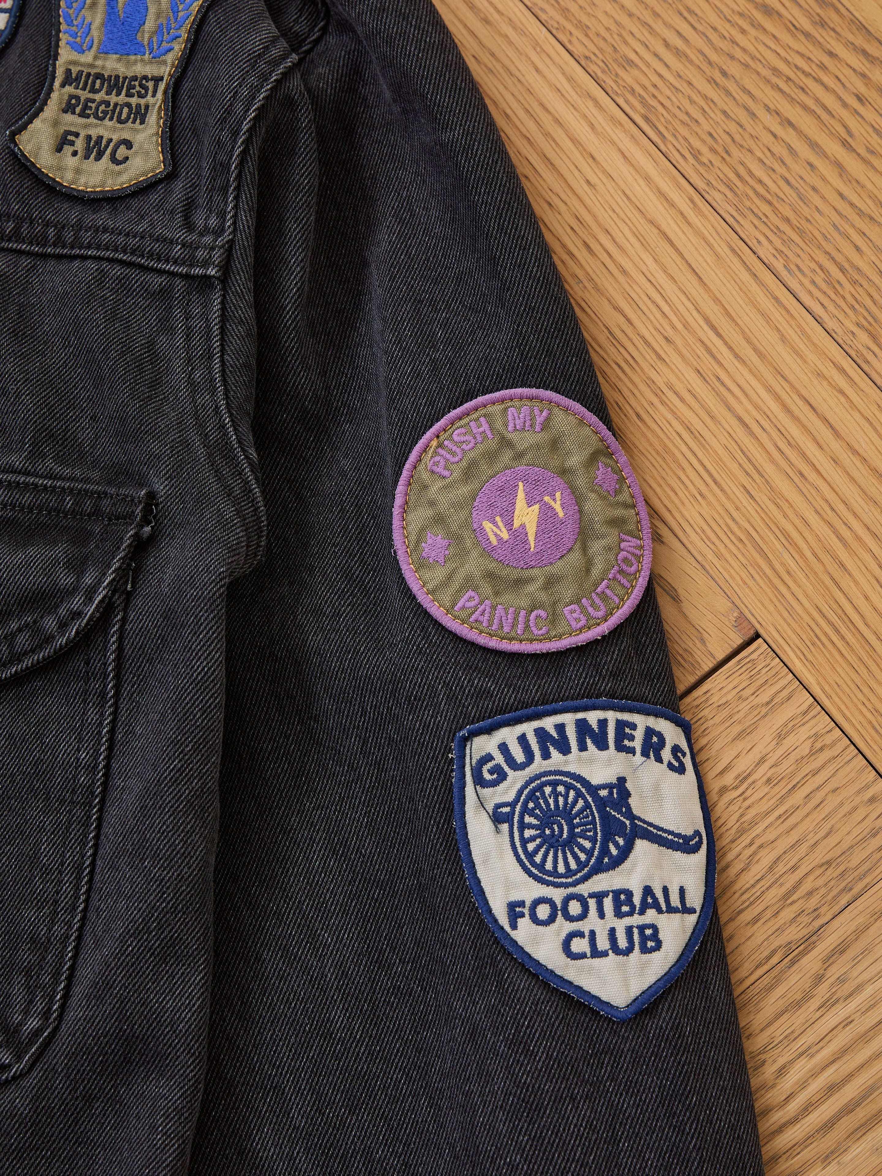 A close-up of the FOUND Denim Patchwork Jacket, a vintage-inspired piece with a corduroy collar and Americana patches: "MIDWEST REGION F.W.C," "RUSH MY PANIC BUTTON," and "GUNNERS FOOTBALL CLUB" on the sleeve.