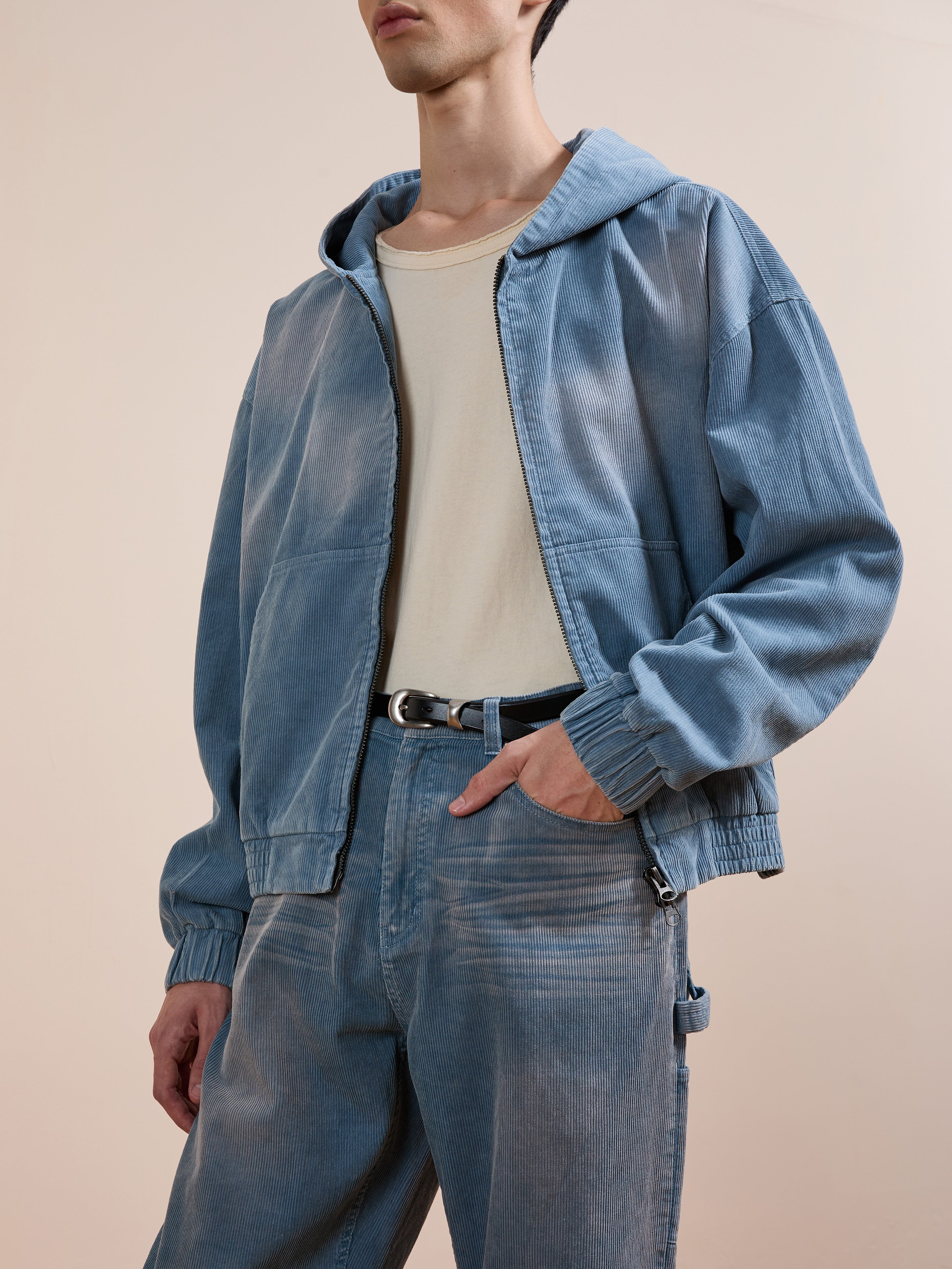 A person layers the FOUND Corduroy Zip Up Hoodie over a light blue denim jacket, cream T-shirt, and matching blue jeans, creating a stylish look against a plain background.