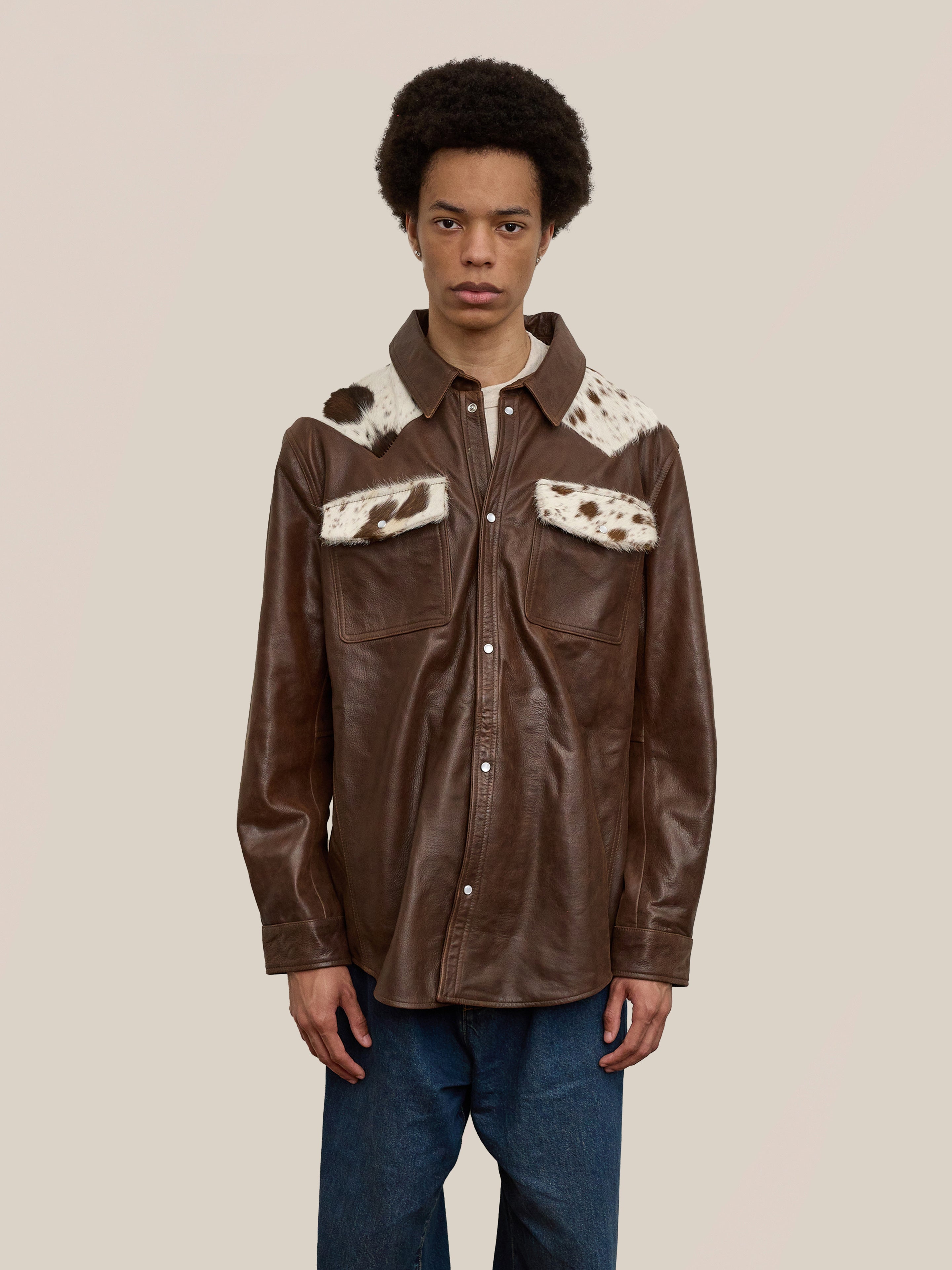 A person wears the FOUND Distressed Leather Cowhide Contrast Western Shirt, featuring white and brown fur accents on the collar and chest pockets, standing against a plain background.