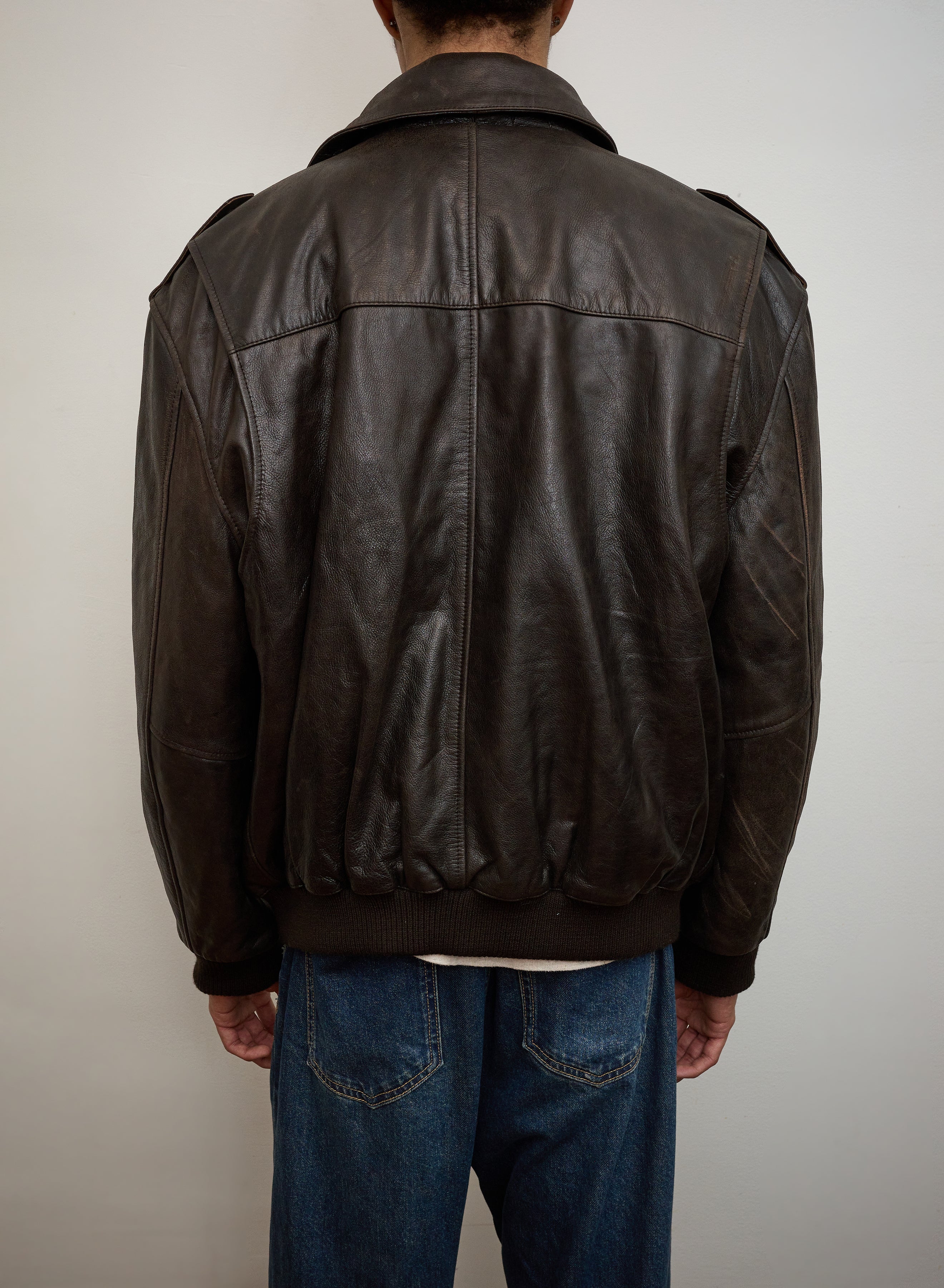 A person wearing the FOUND Distressed Leather Flight Jacket and blue jeans is photographed from the back against a plain light-colored wall.