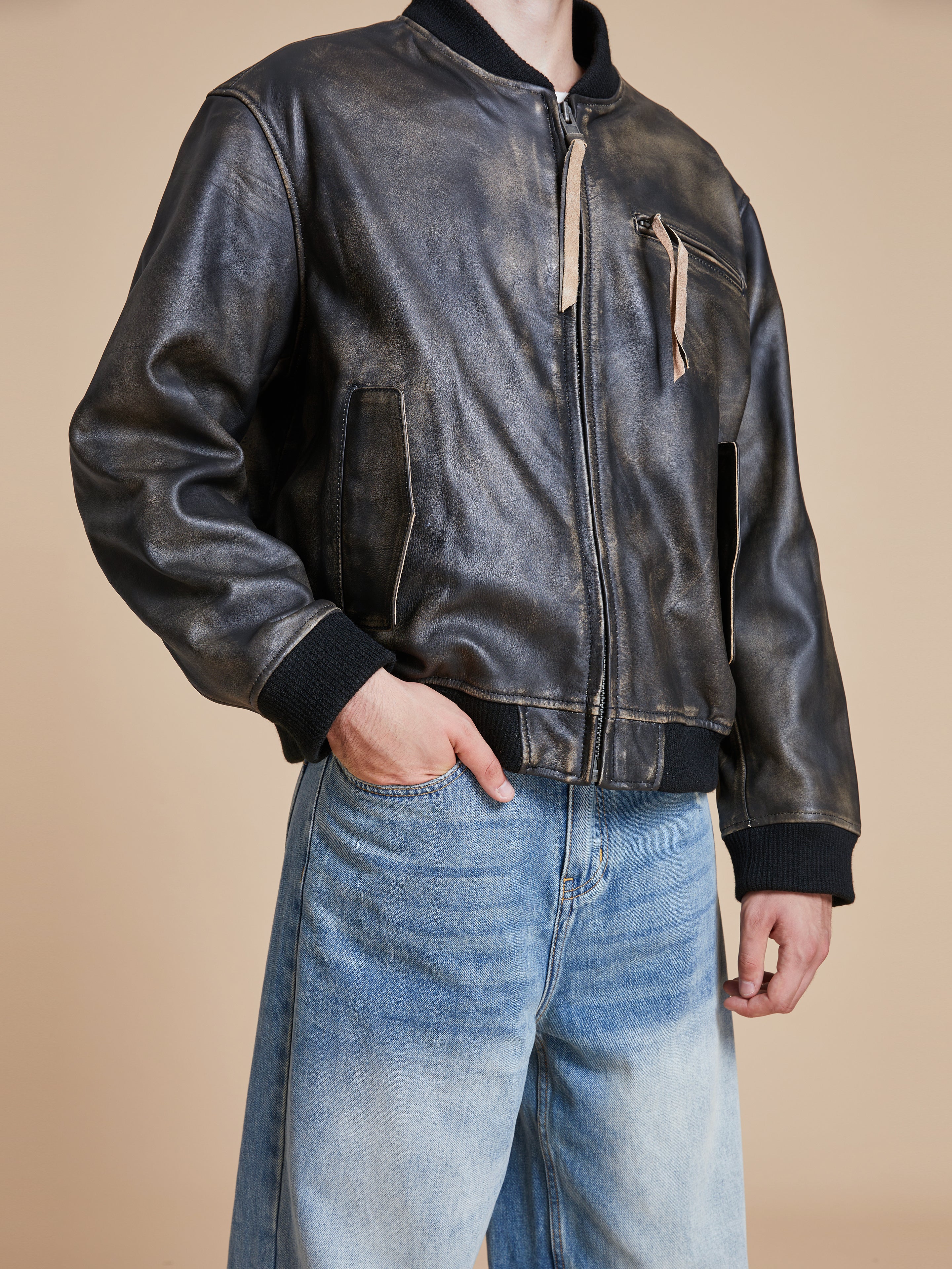 A man wearing a Found Distressed Pavement Leather Bomber Jacket and jeans.