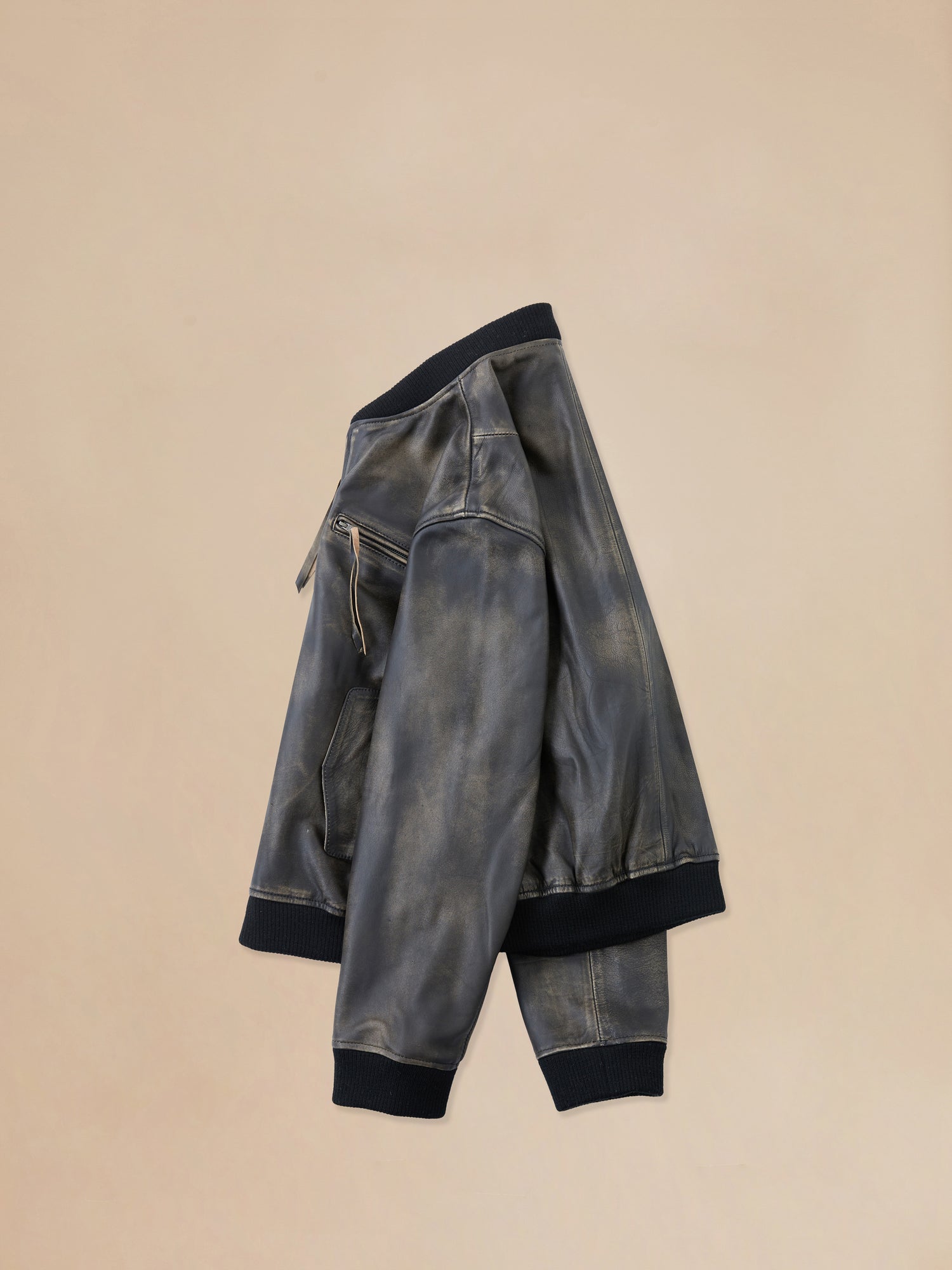 A pair of Distressed Pavement Leather Bomber Jacket by Found on a beige surface.