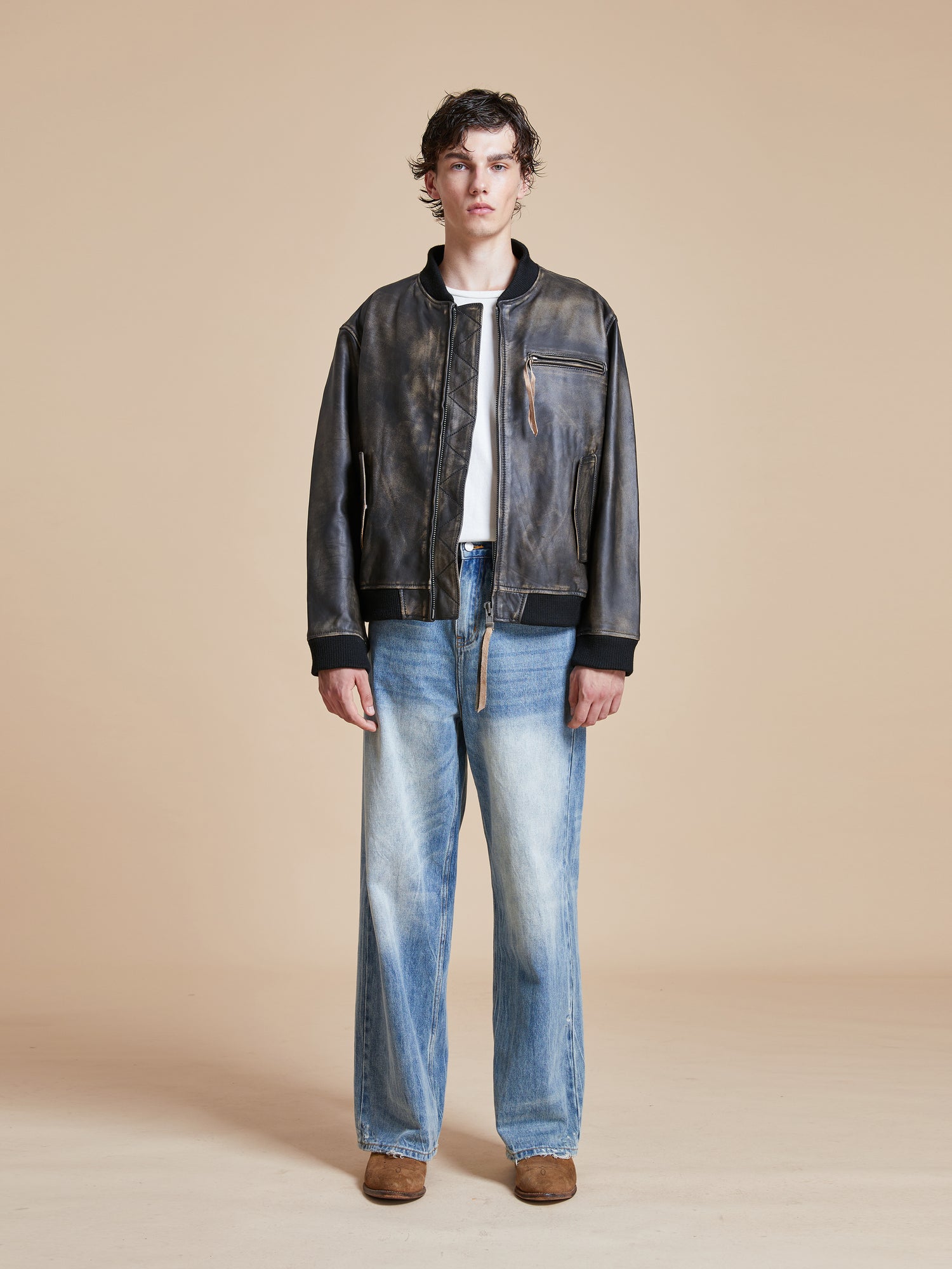 A man wearing jeans and a Found Distressed Pavement Leather Bomber Jacket.