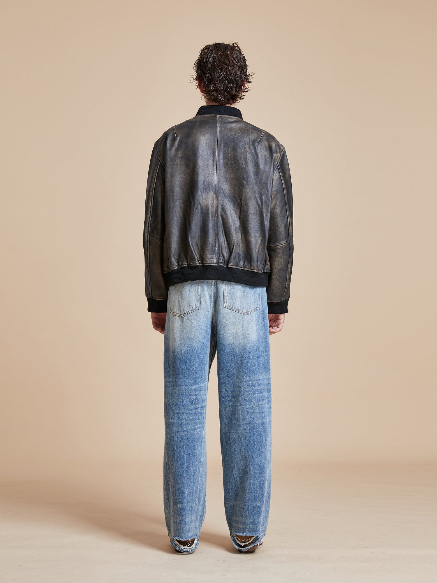 The back view of a man wearing jeans and a Found Distressed Pavement Leather Bomber Jacket.