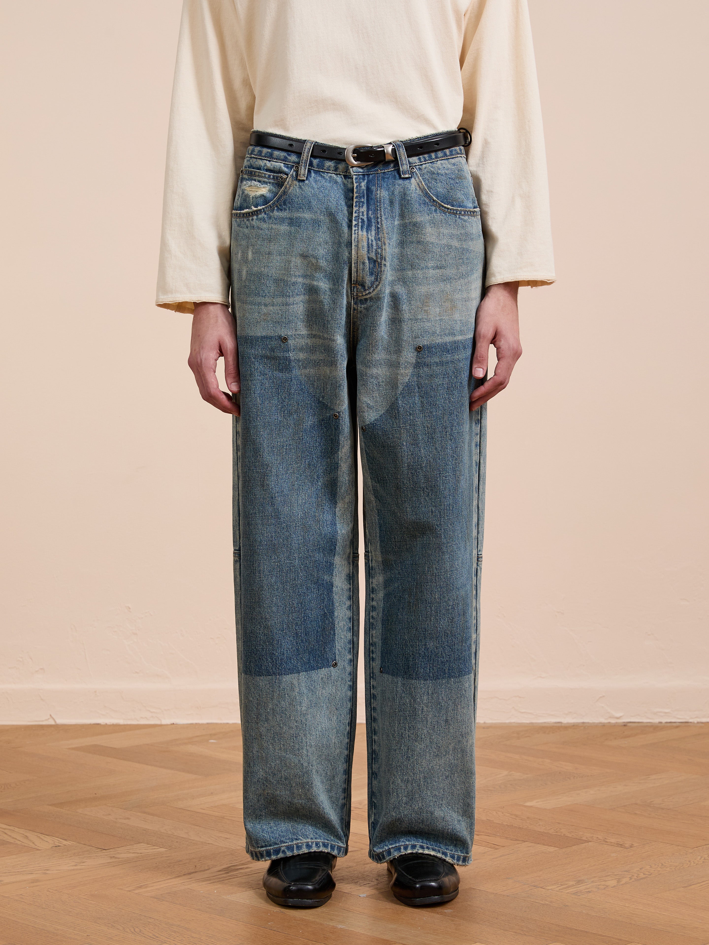 Person wearing a long-sleeved cream shirt, FOUND Double Knee Carpenter Jeans with a black belt, and black shoes, standing on a wooden floor against a plain light-colored wall.