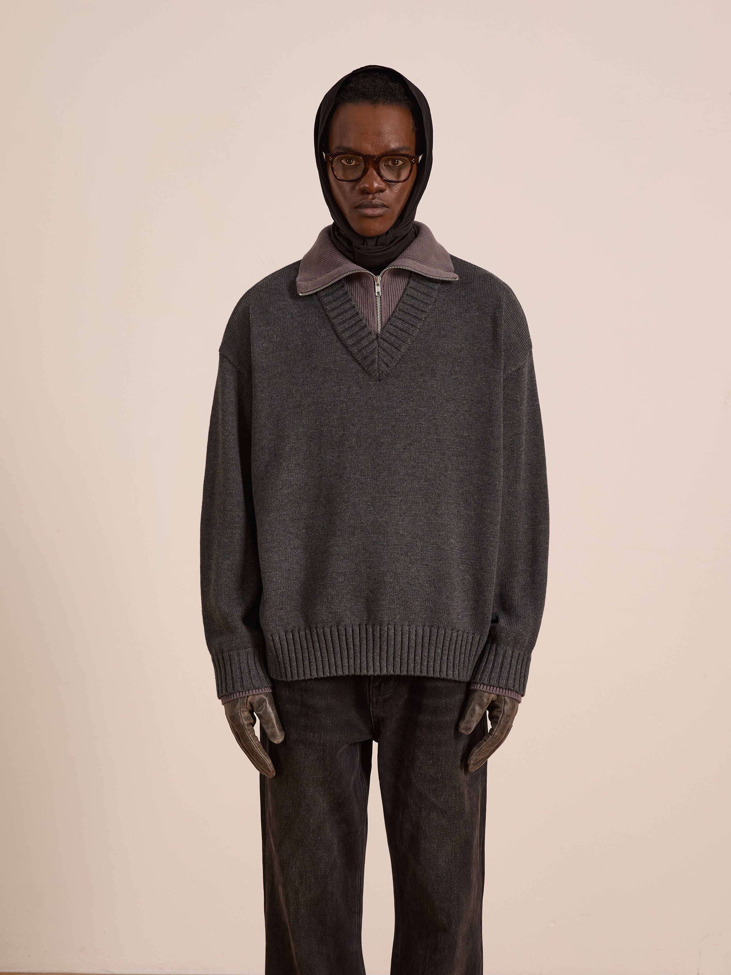 A person stands against a plain background wearing the FOUND Double Layer Sweater in gray over a collared shirt, paired with dark pants, gloves, glasses, and a headscarf—ideal for cold-weather layering.