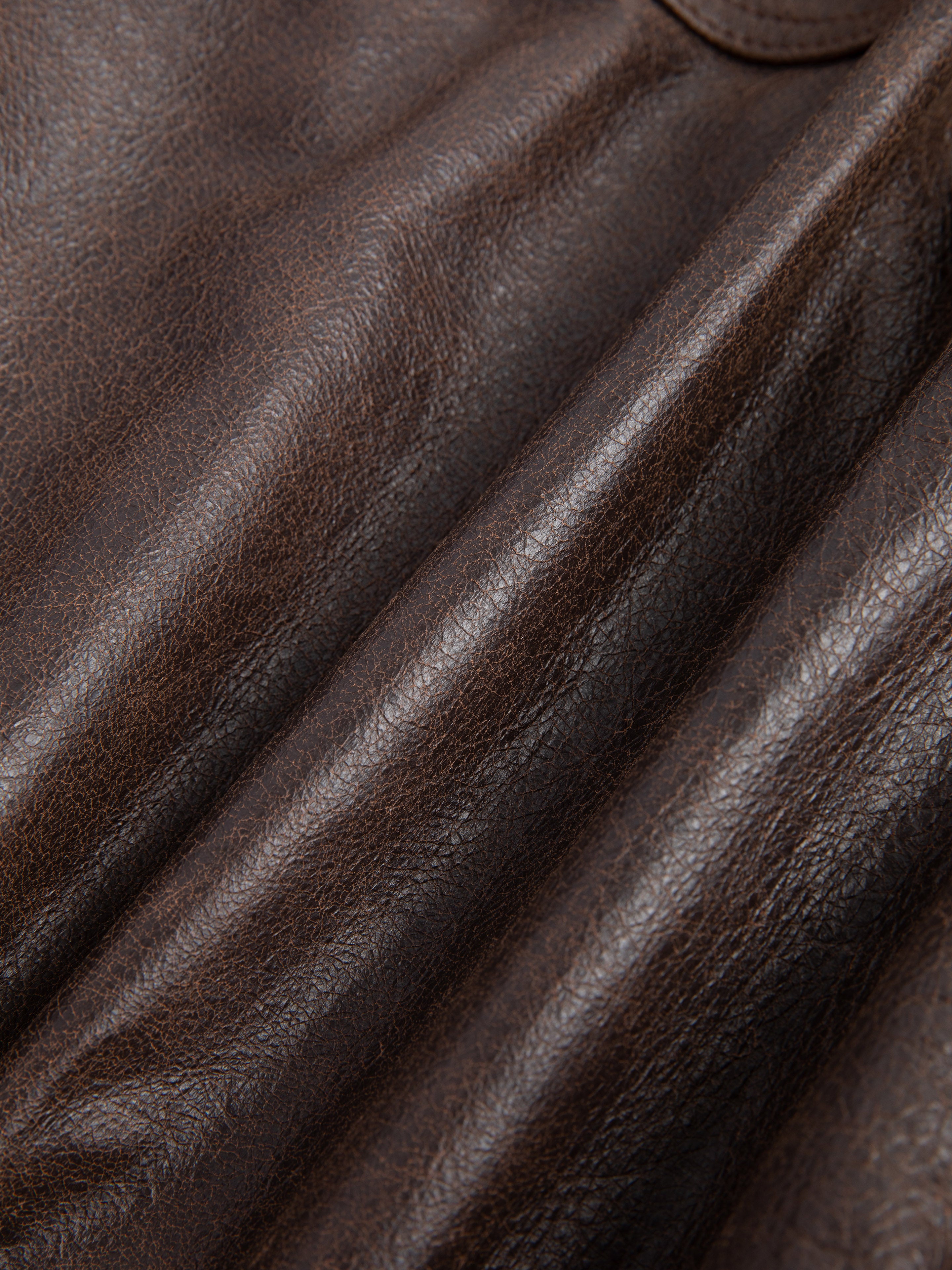 Close-up of dark brown, ethically sourced leather with visible creases and grain patterns from Found's Dusk Distressed Genuine Leather Cargo Shorts.