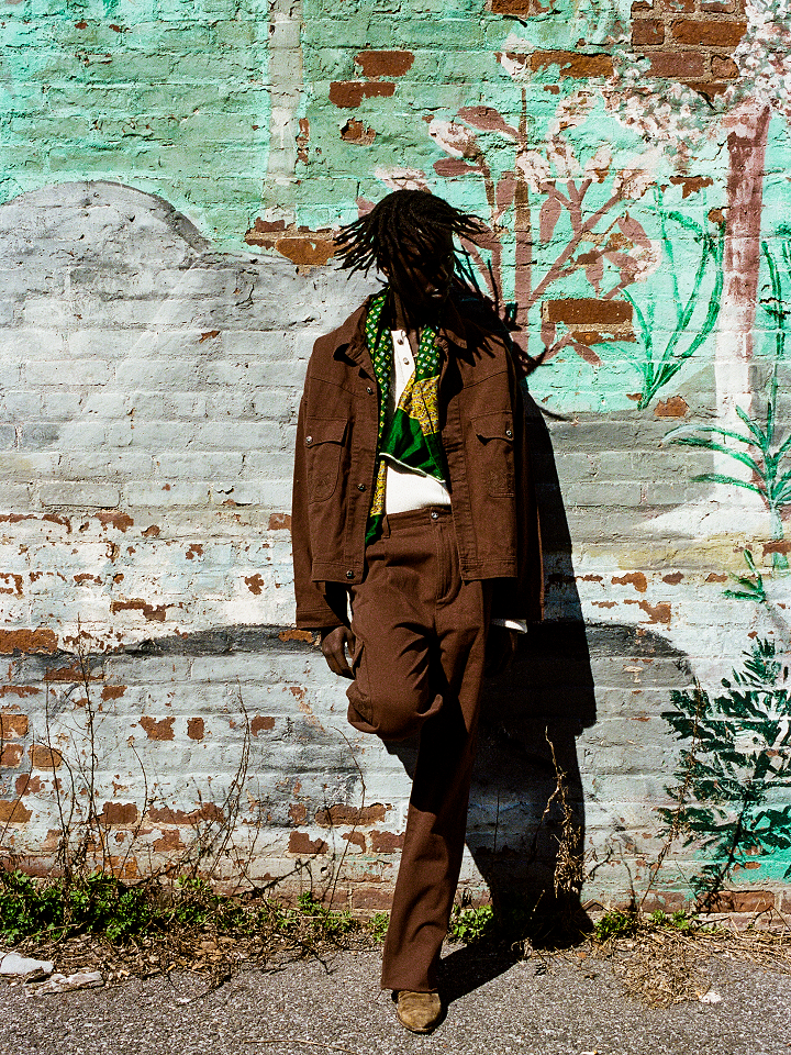 A man with dreadlocks leaning against a brick wall wearing Dusky Western Cargo Jeans by Found.