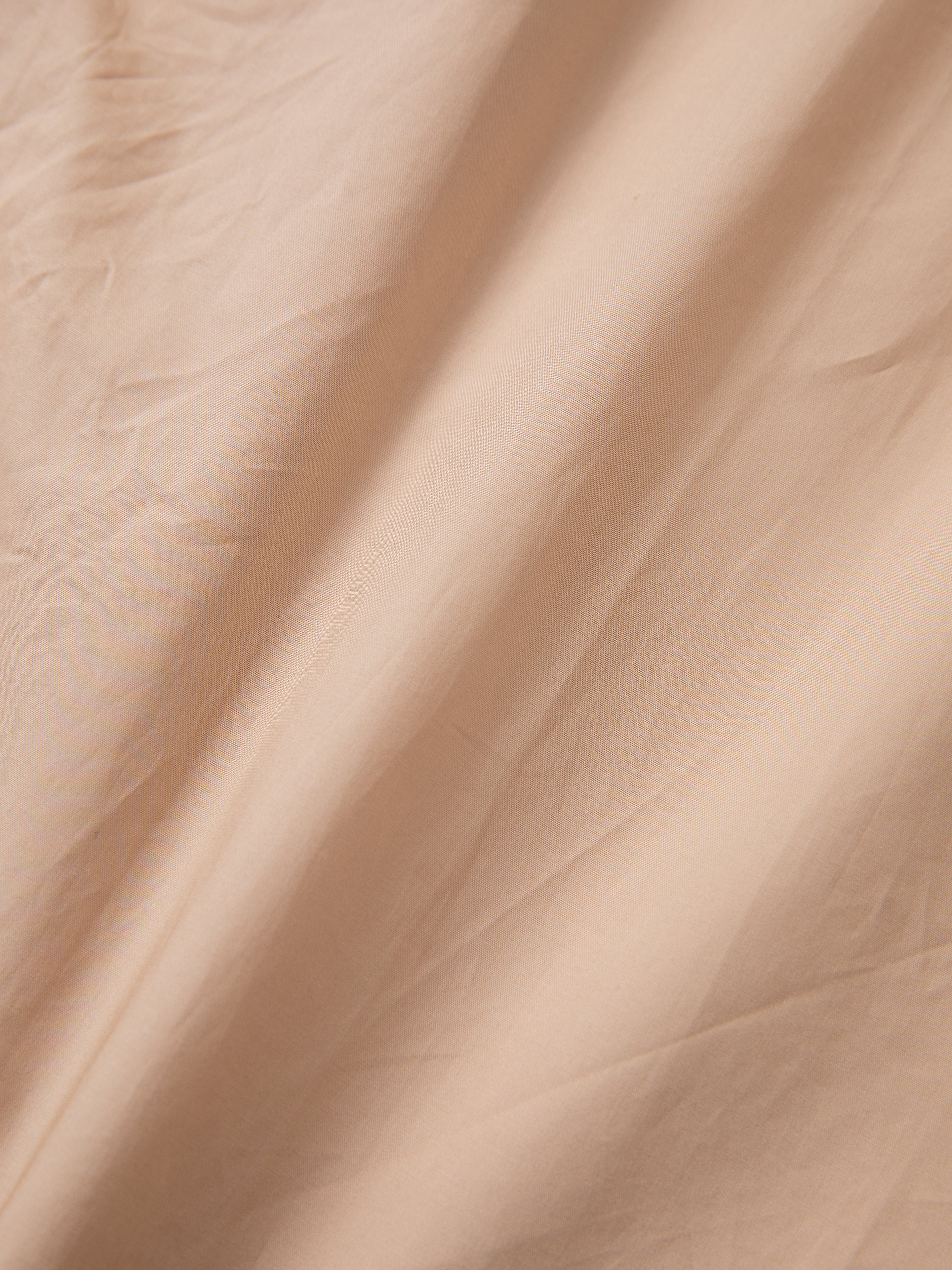 A close-up view of the "Embroidered Western Button Up" by FOUND showcasing its beige fabric with visible creases and a smooth texture.