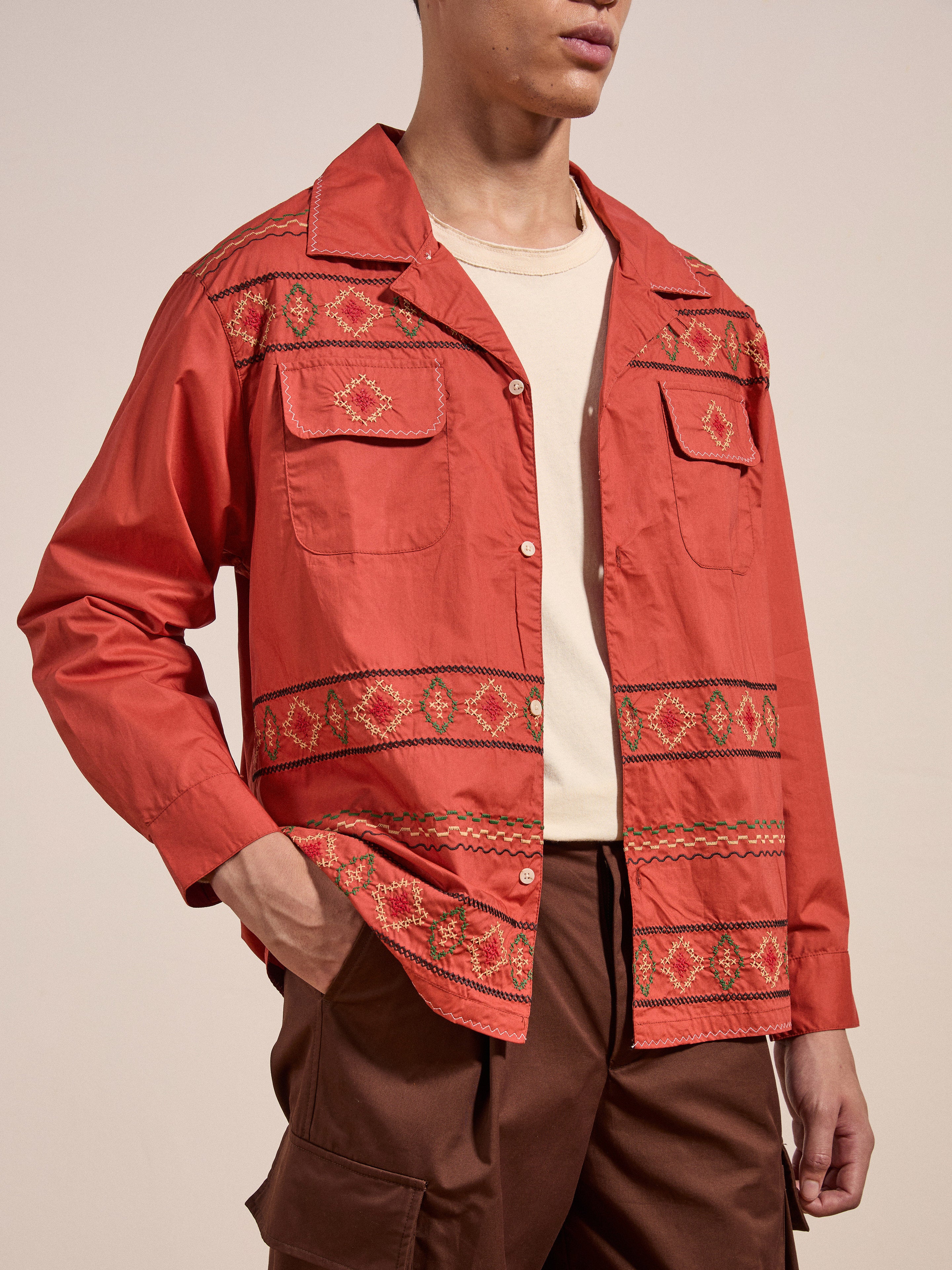 A person wearing the Embroidered Western Button Up by FOUND, featuring intricate embroidery, stands against a plain background. They have one hand in the pocket of their brown cargo pants and are partially turned to the side.