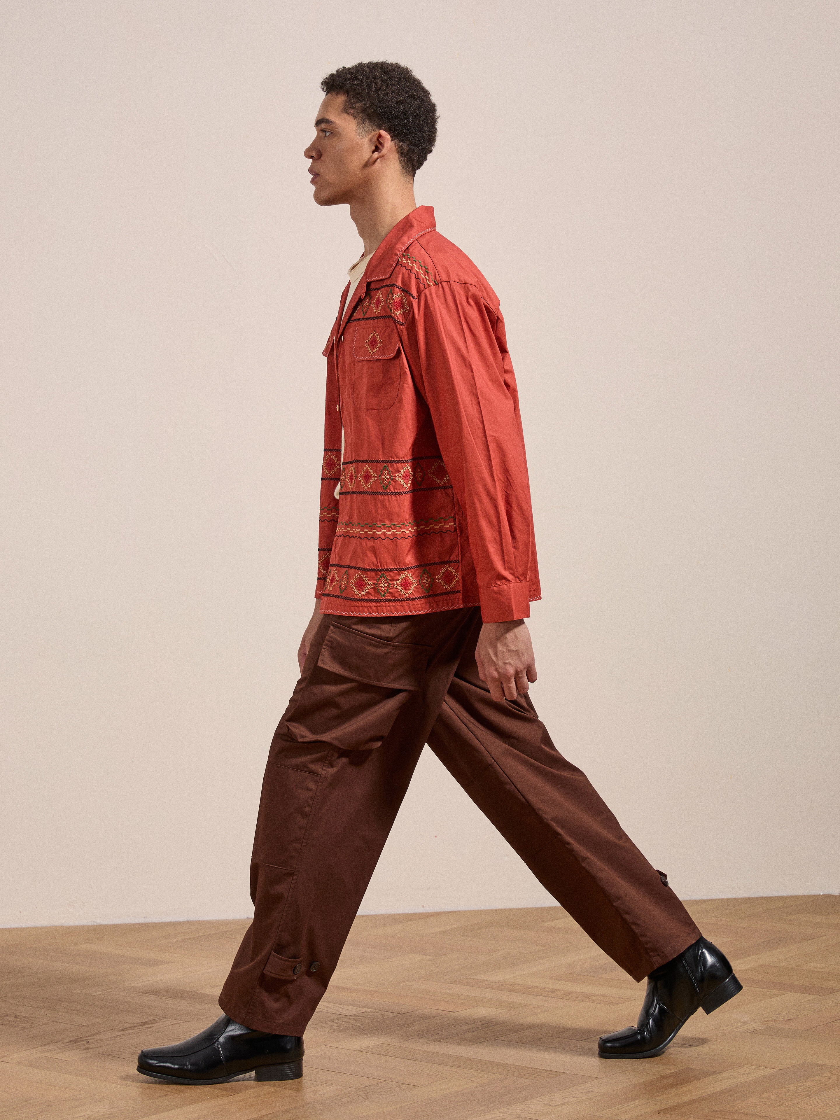 A person wearing a FOUND Embroidered Western Button Up and brown pants walks in profile across a wooden floor.