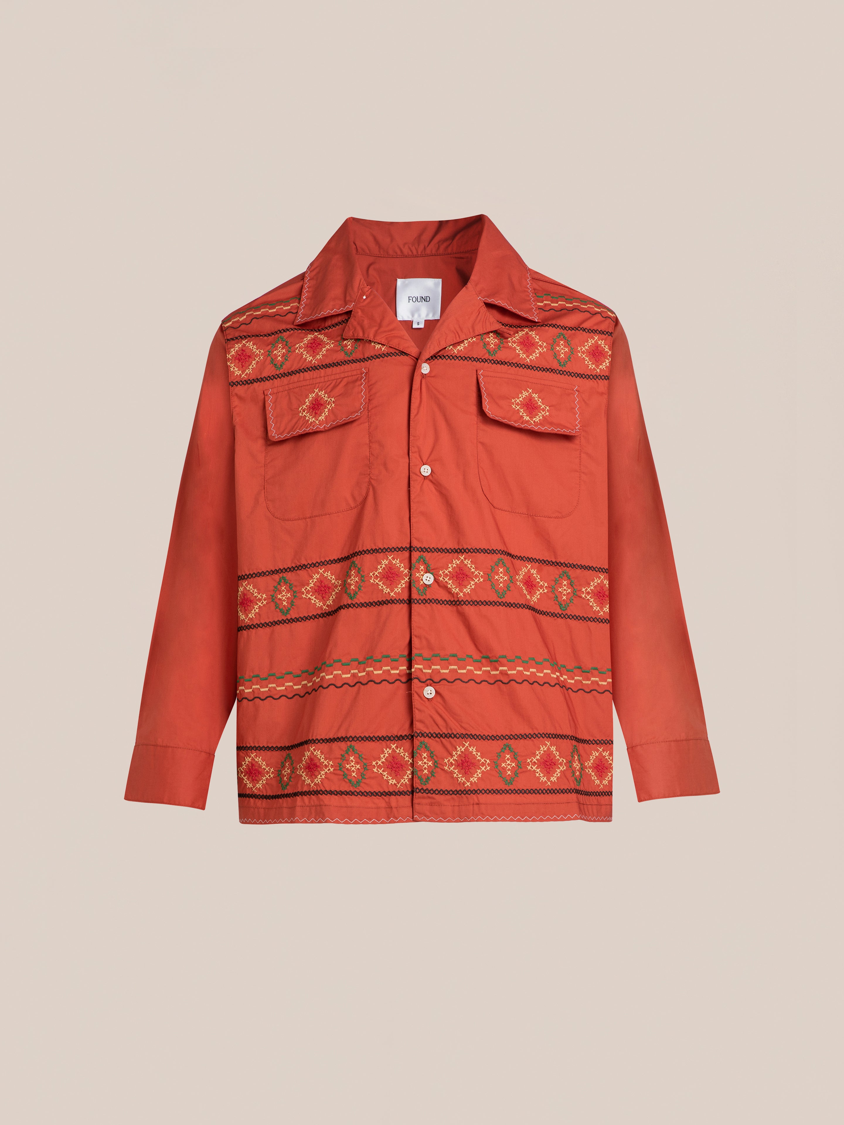 The Embroidered Western Button Up from FOUND is a red shirt with a collar, featuring patterned, colorful horizontal stripes across the chest, pockets, and lower torso. It also includes two chest pockets.