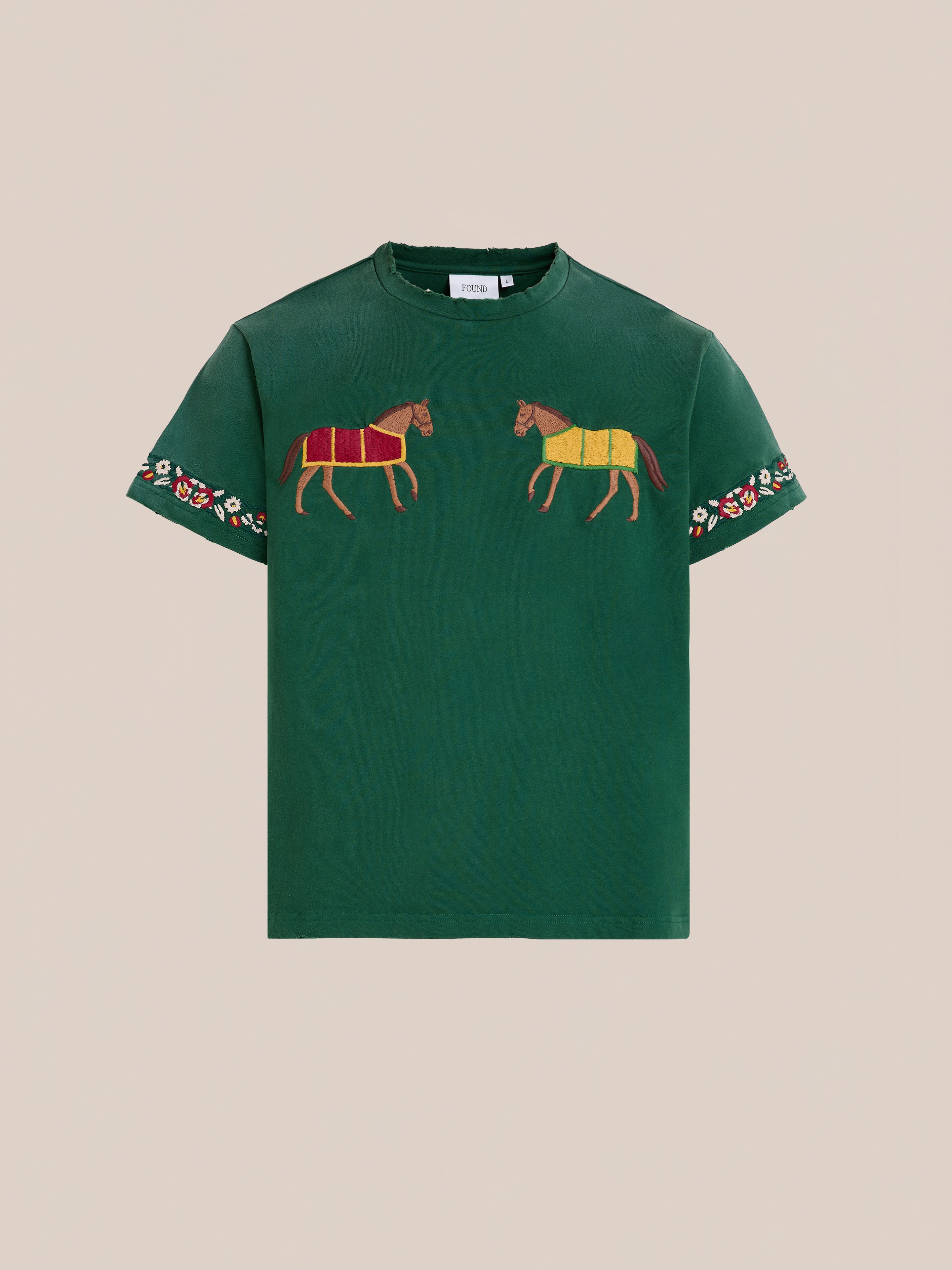 The FOUND Horse Equine Tee is a green short-sleeve shirt featuring embroidered horses on the chest and floral embroidery on the sleeves, shown against a plain beige background.
