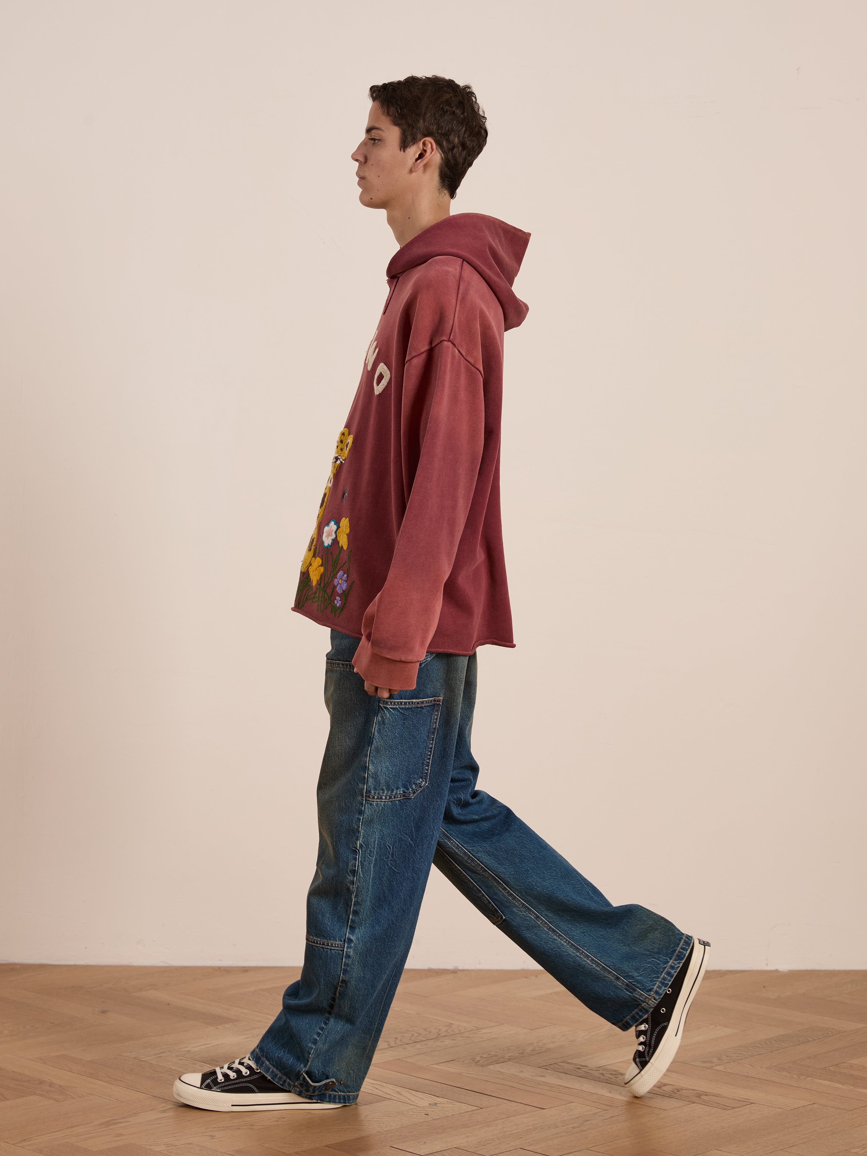 Wearing a FOUND Embroidered Wildlife Hoodie in vibrant red paired with blue wide-leg jeans, a person walks across the wooden floor.