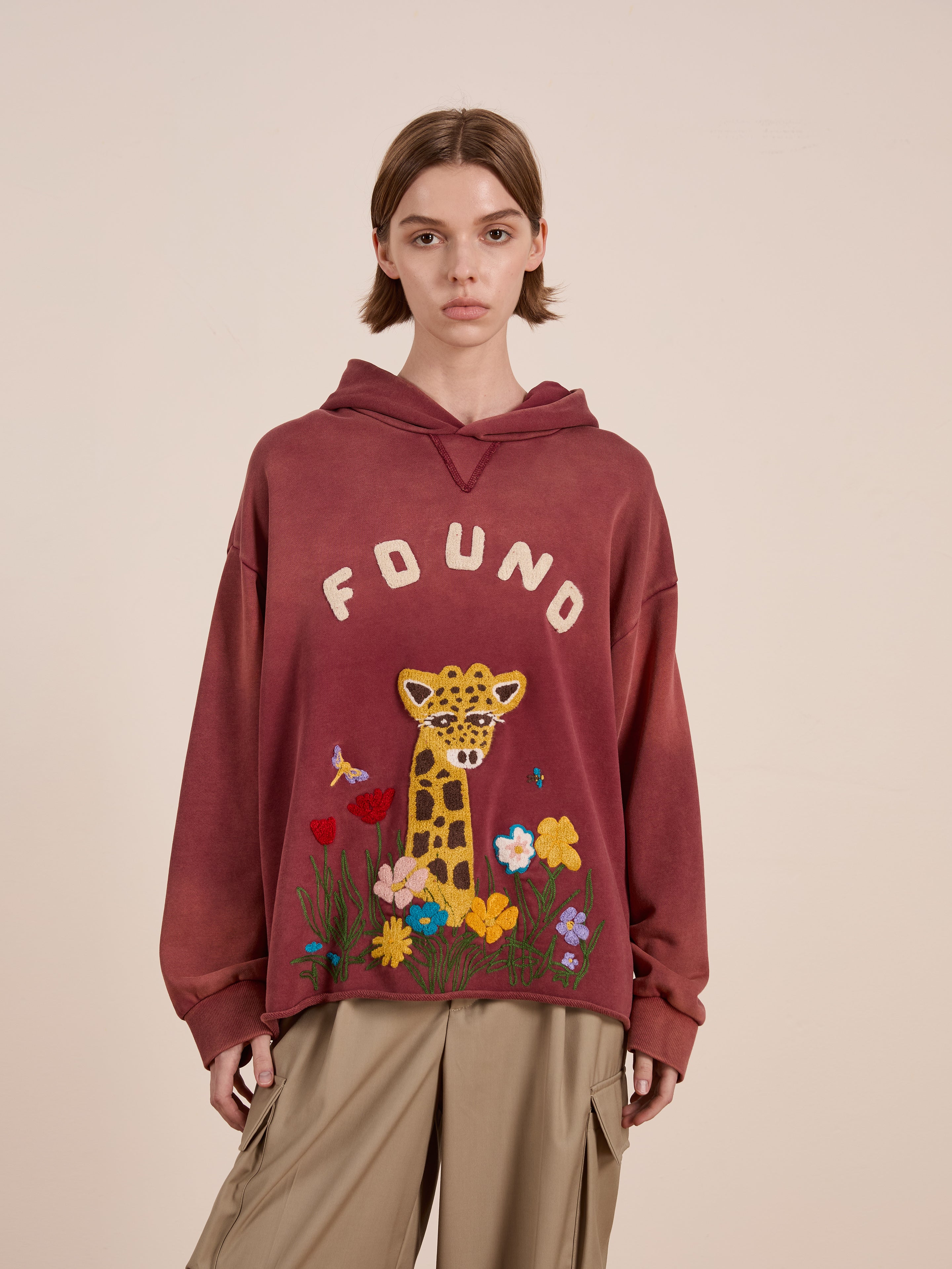 A model dons the FOUND brand's Embroidered Wildlife Hoodie, a red unisex relaxed fit featuring vibrant leopard and floral designs, epitomizing nature's fierce elegance.