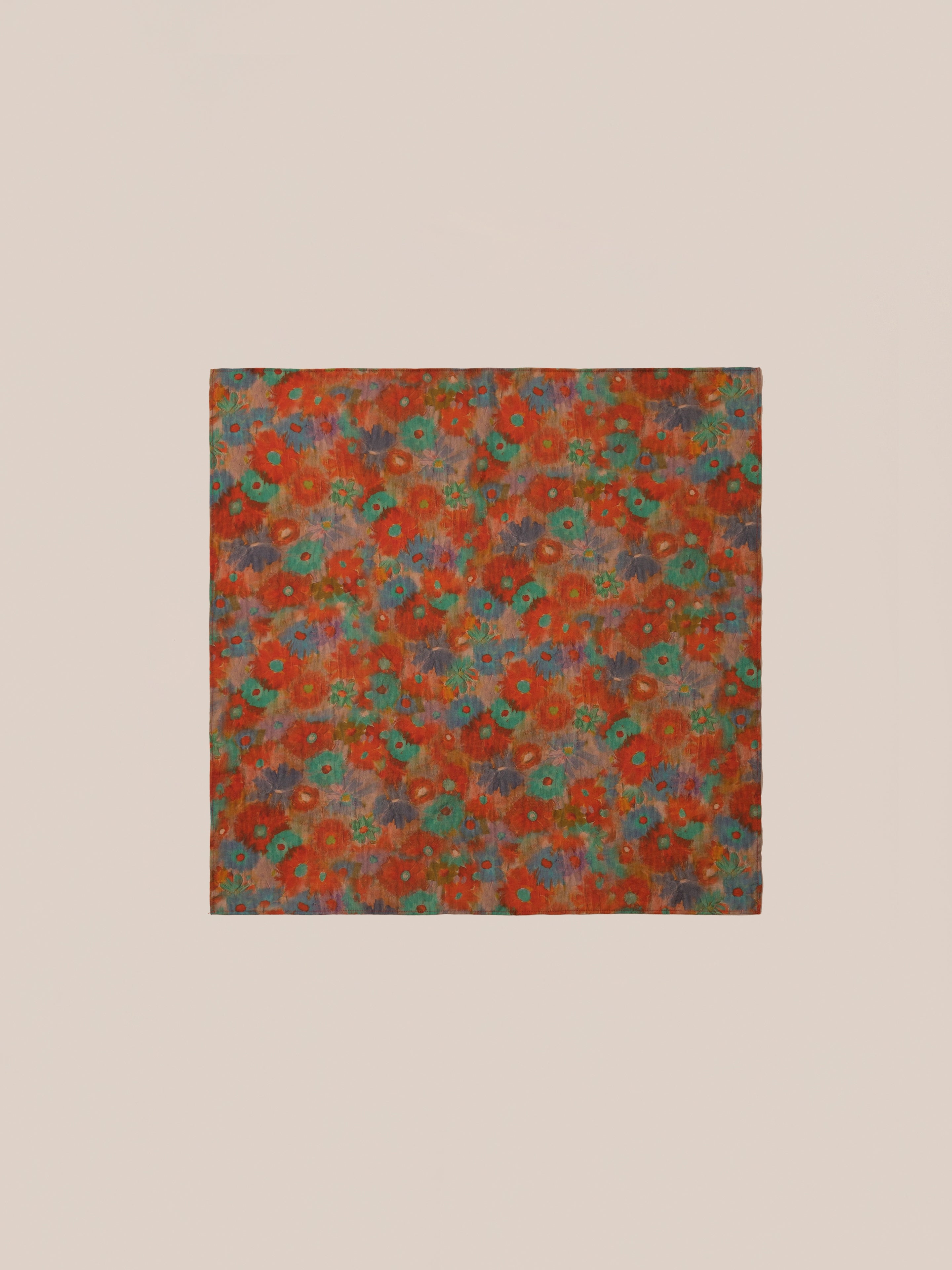 The Sepehr Bandana by FOUND is a square fabric adorned with a vibrant floral pattern featuring red, green, and orange hues set against a light beige background.