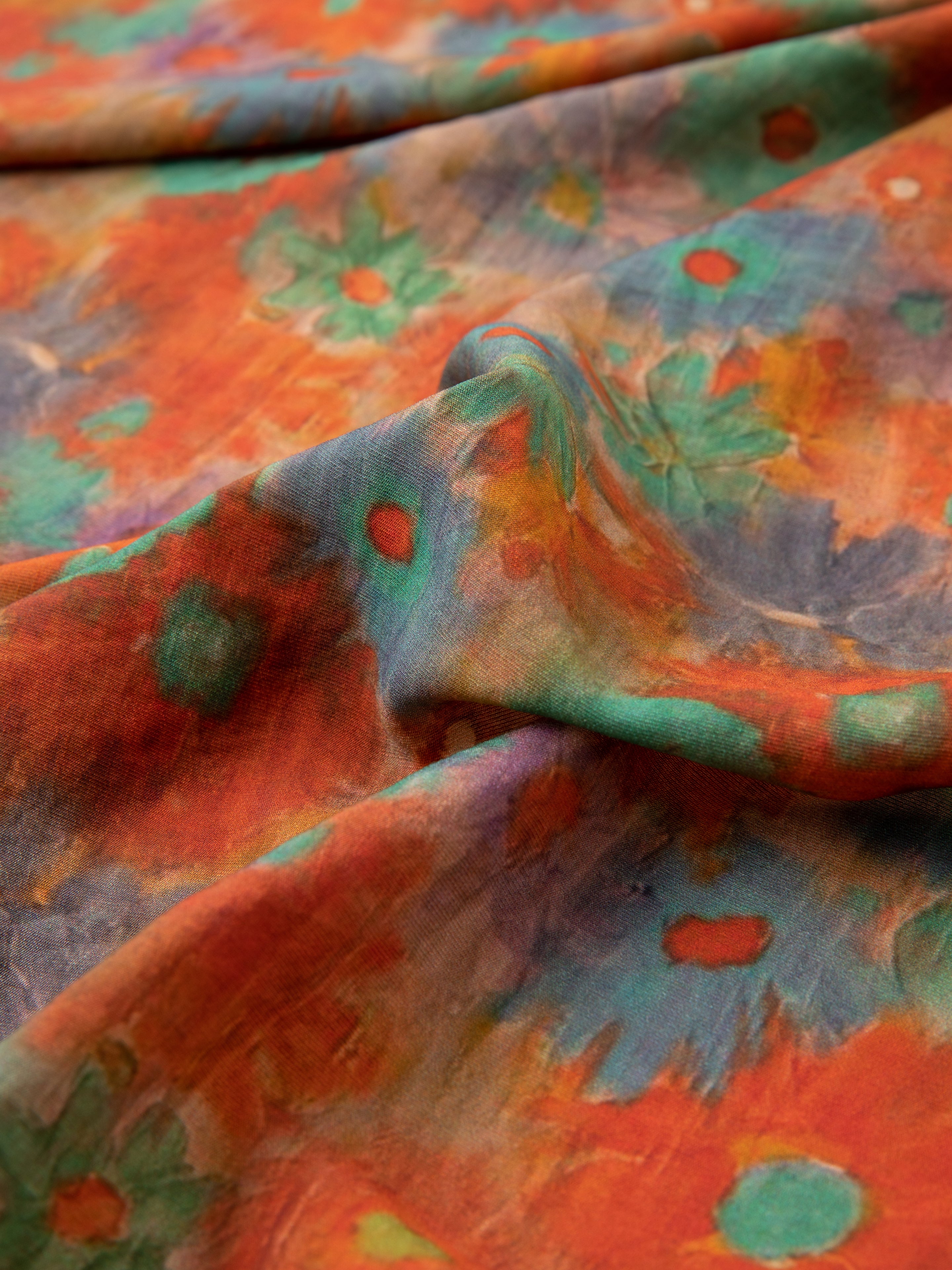 Close-up image of the Sepehr Bandana by FOUND, showcasing a colorful abstract floral pattern in shades of orange, blue, green, and red. The fabric has soft folds and creases.