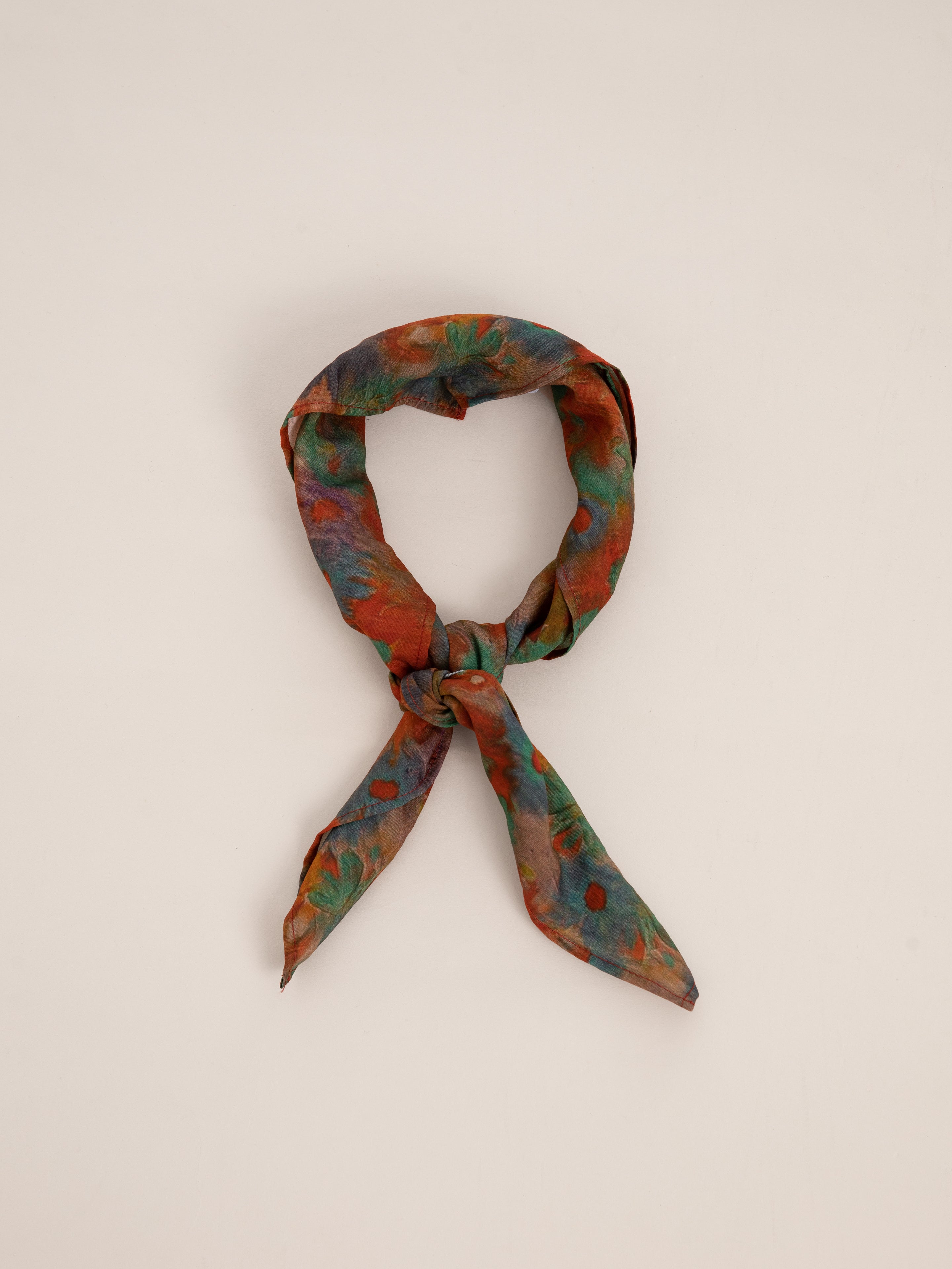 A Sepehr Bandana from FOUND, featuring a twisted and multicolored floral pattern tied in a simple knot against a plain background.