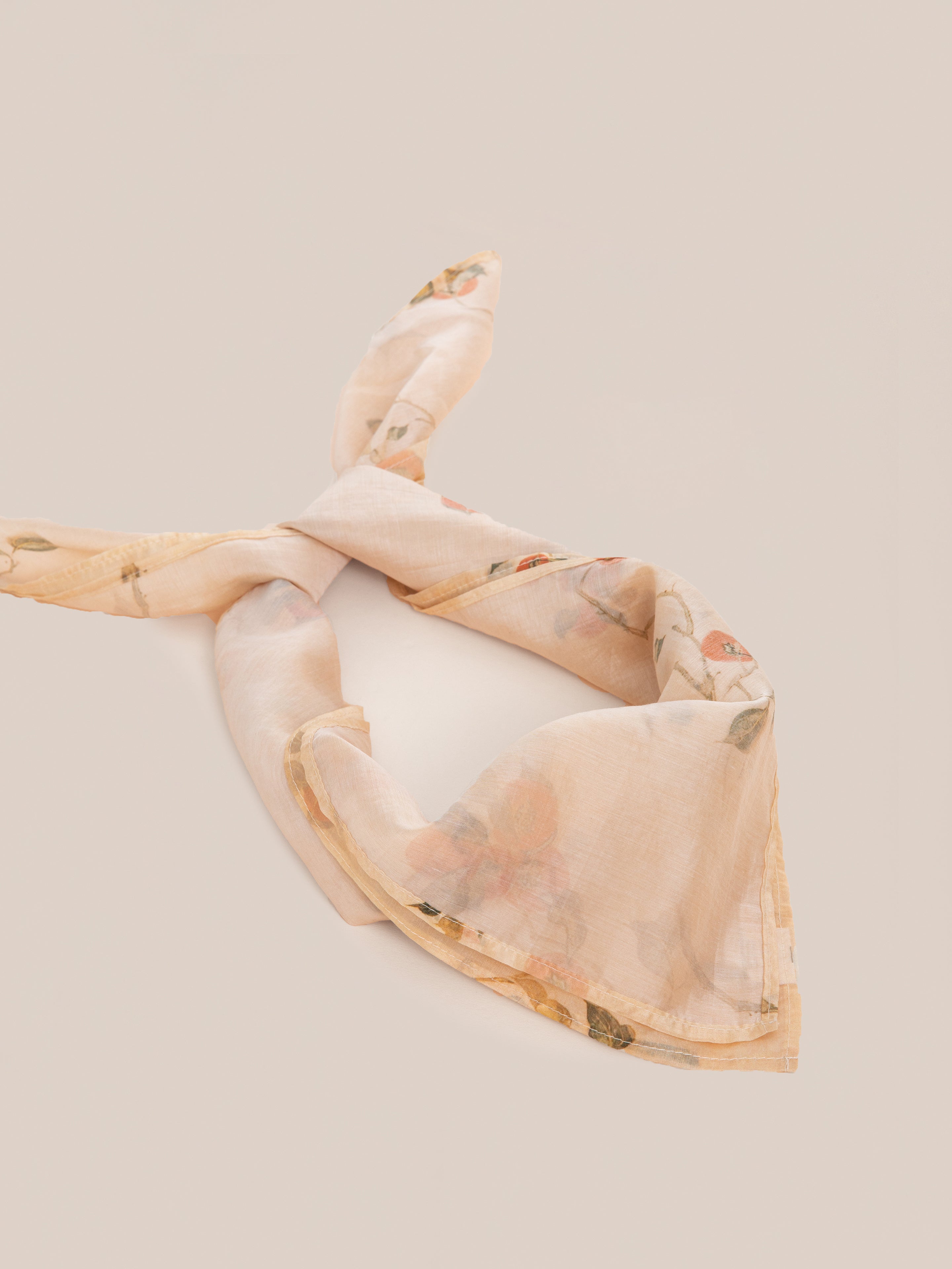 A Roshan Floral Bandana by FOUND, featuring light pastel tones and floral patterns, is laid out in a loose knot on a plain background.