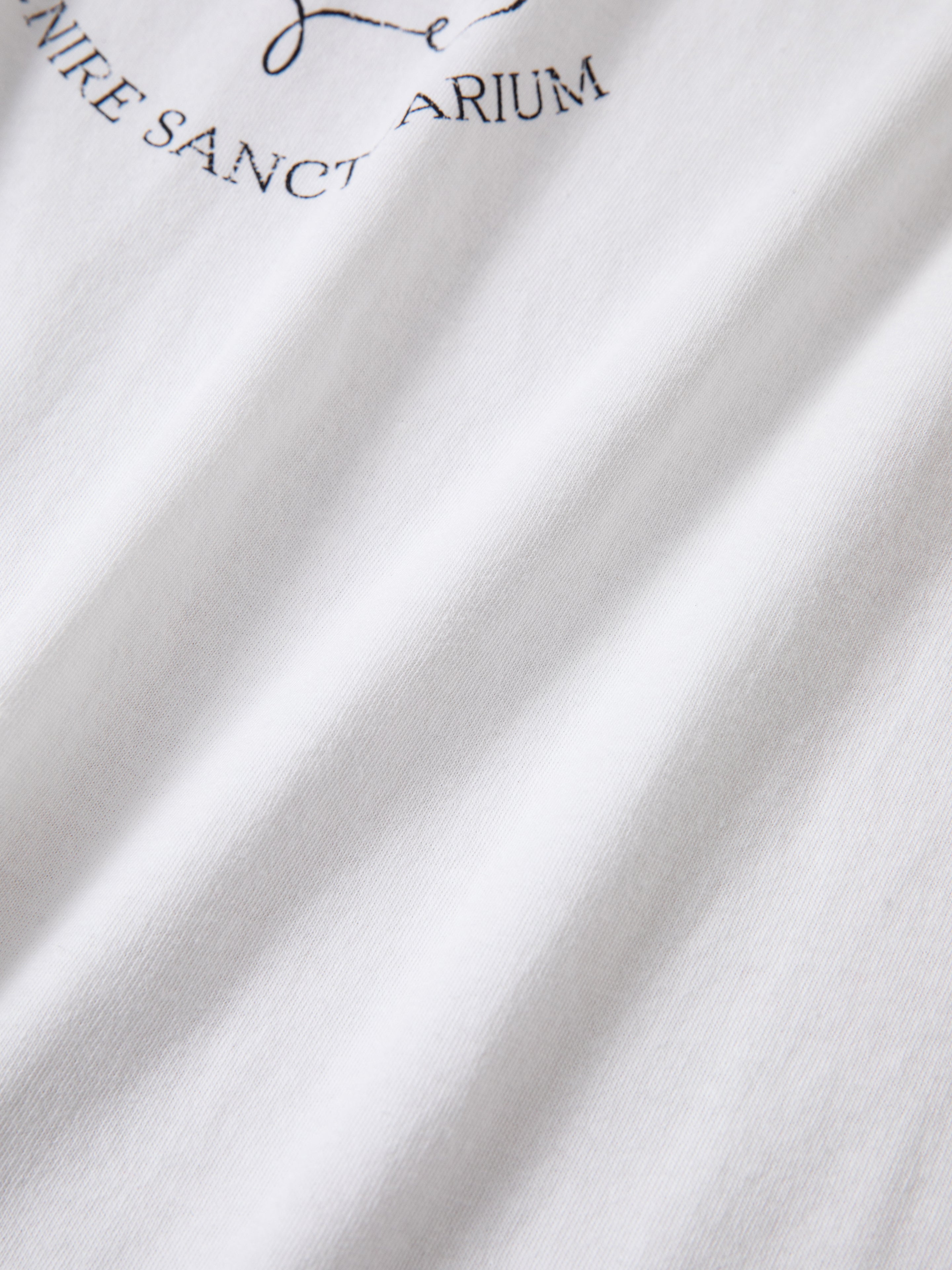 Close-up of white fabric with partial black text including the words "SANCT" and "ARIUM," featuring a distressed screen print on this 100% cotton Horse Crest Ringer Tee by FOUND.