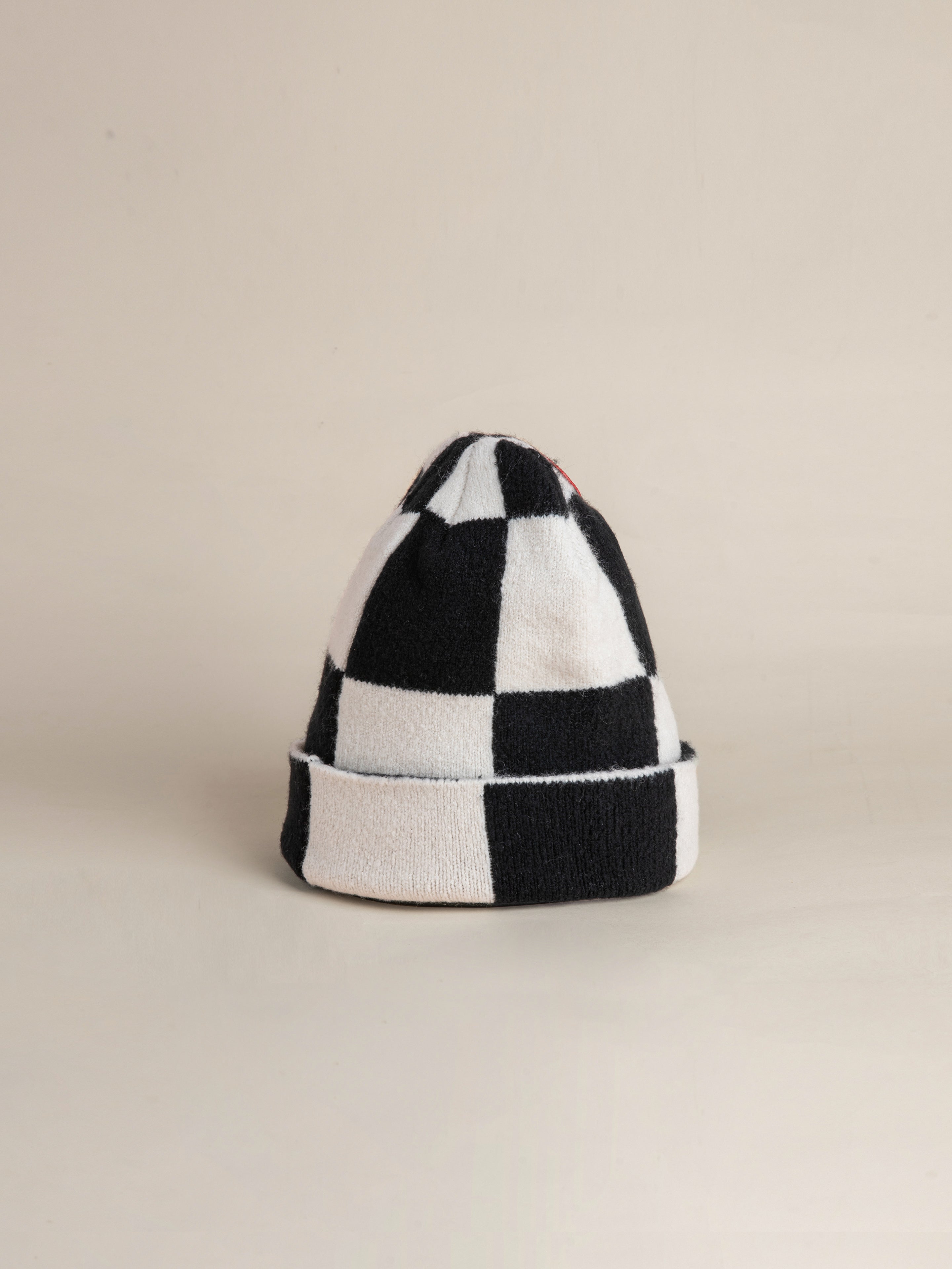 A Check Multi Patch Beanie by FOUND, showcasing a black and white checkered design, rests against a neutral background with its base folded neatly.