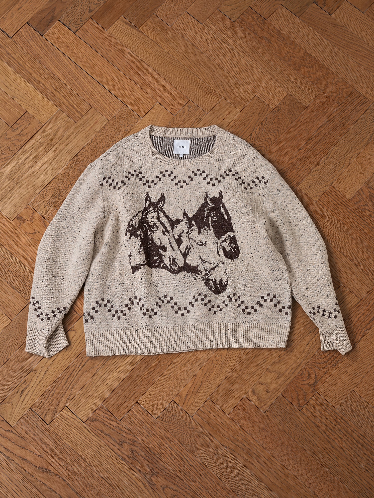 Speckled Knit Horse Sweater by FOUND featuring a beige jacquard horse design and decorative patterns in an oversized fit, displayed on a wooden floor.