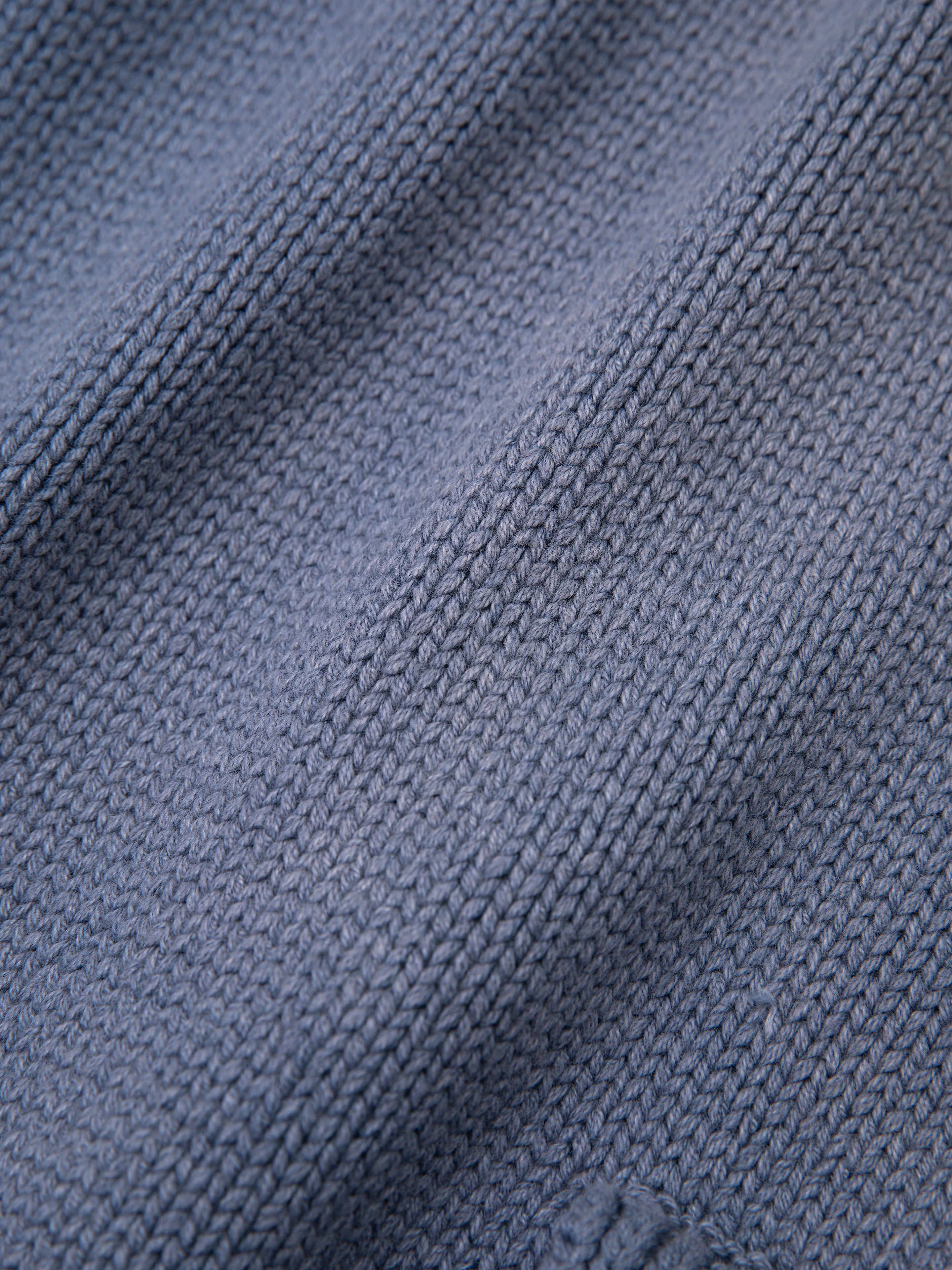 Close-up of a textured blue fabric with a woven pattern, reminiscent of the intricate details found in the Faded Knit Pocket Hoodie by FOUND, showcasing fine details and subtle color variations.