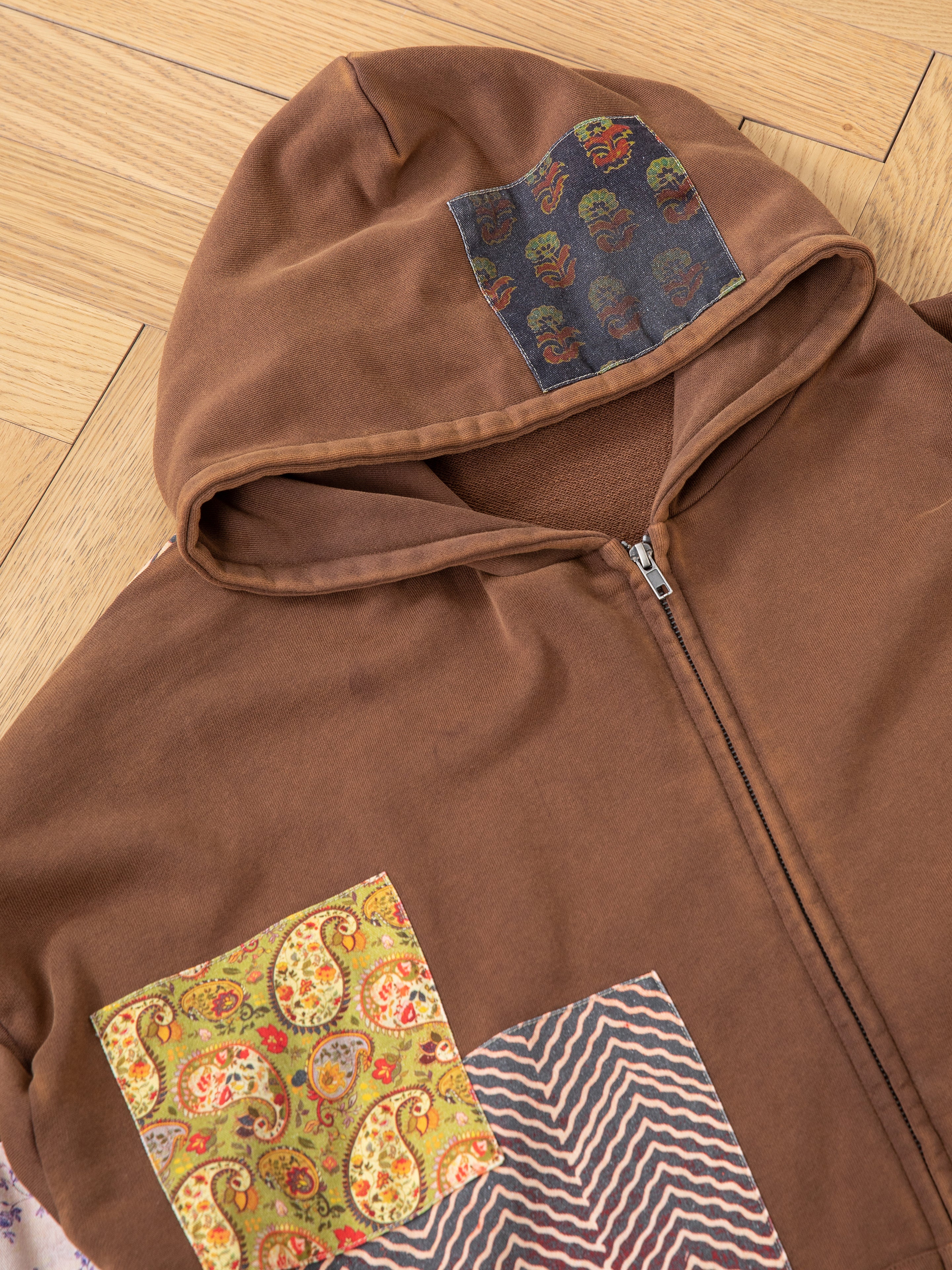 The Tapestry Patchwork Zip Up Hoodie by FOUND showcases an eclectic blend of South Asian tapestry-inspired fabric patches, featuring paisley and zigzag designs for a distinctive oversized look.