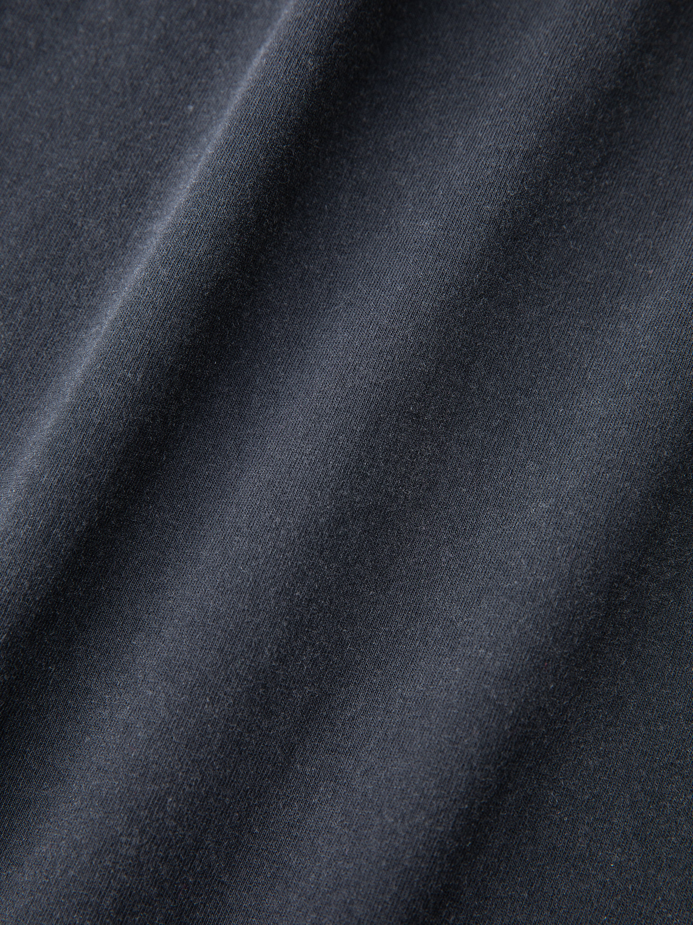 Close-up of the textured, dark gray fabric with diagonal folds from the Studded LS Shirt by FOUND.