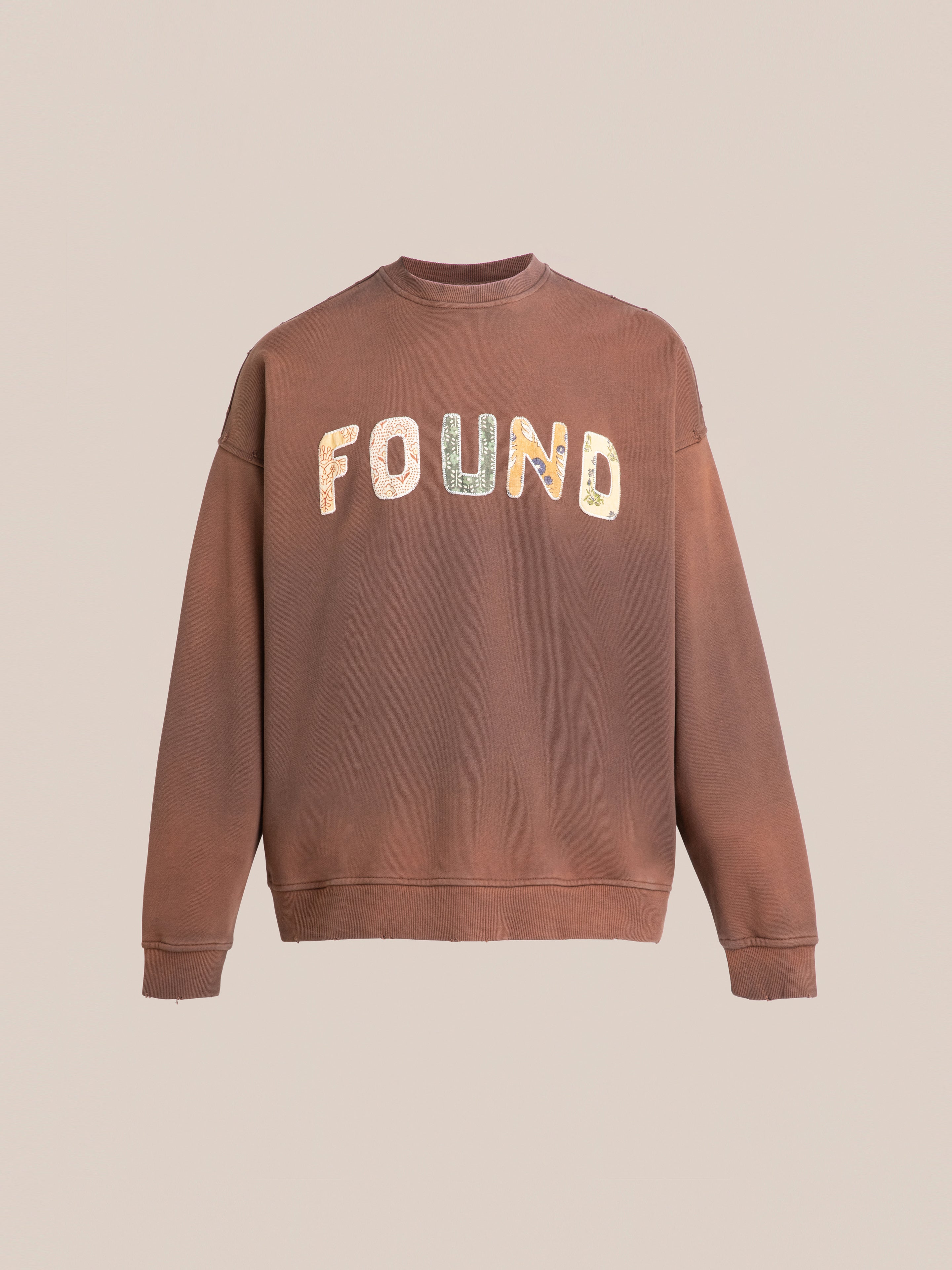 The Patterned Logo Crewneck by FOUND is a brown sweatshirt with "FOUND" in multicolored block letters on the front, made from soft french terry cotton against a plain background.