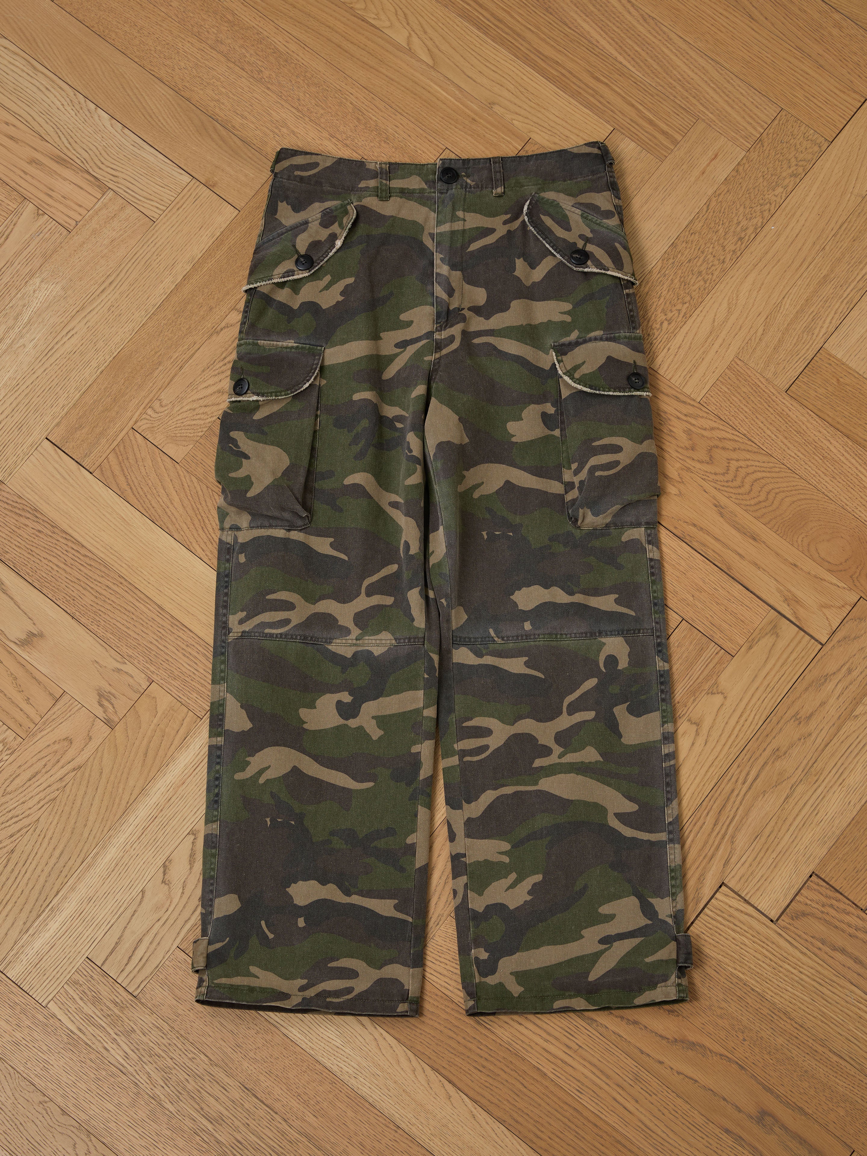 Camouflage Twill Utility Cargo Pants from FOUND, featuring a vintage look and multiple pockets, rest on a wooden herringbone-patterned floor.