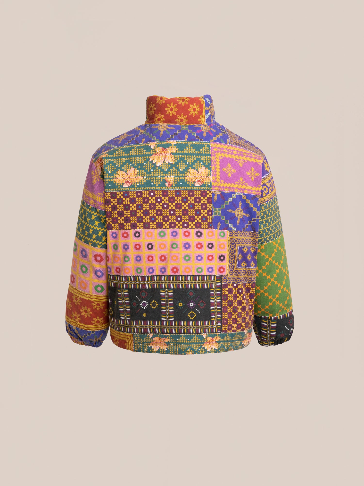 The Ayubia Printed Tapestry Puffer Jacket by FOUND showcases a back view with multicolored, patchwork designs featuring an array of floral and geometric patterns on a beige background, inspired by South Asian prints.