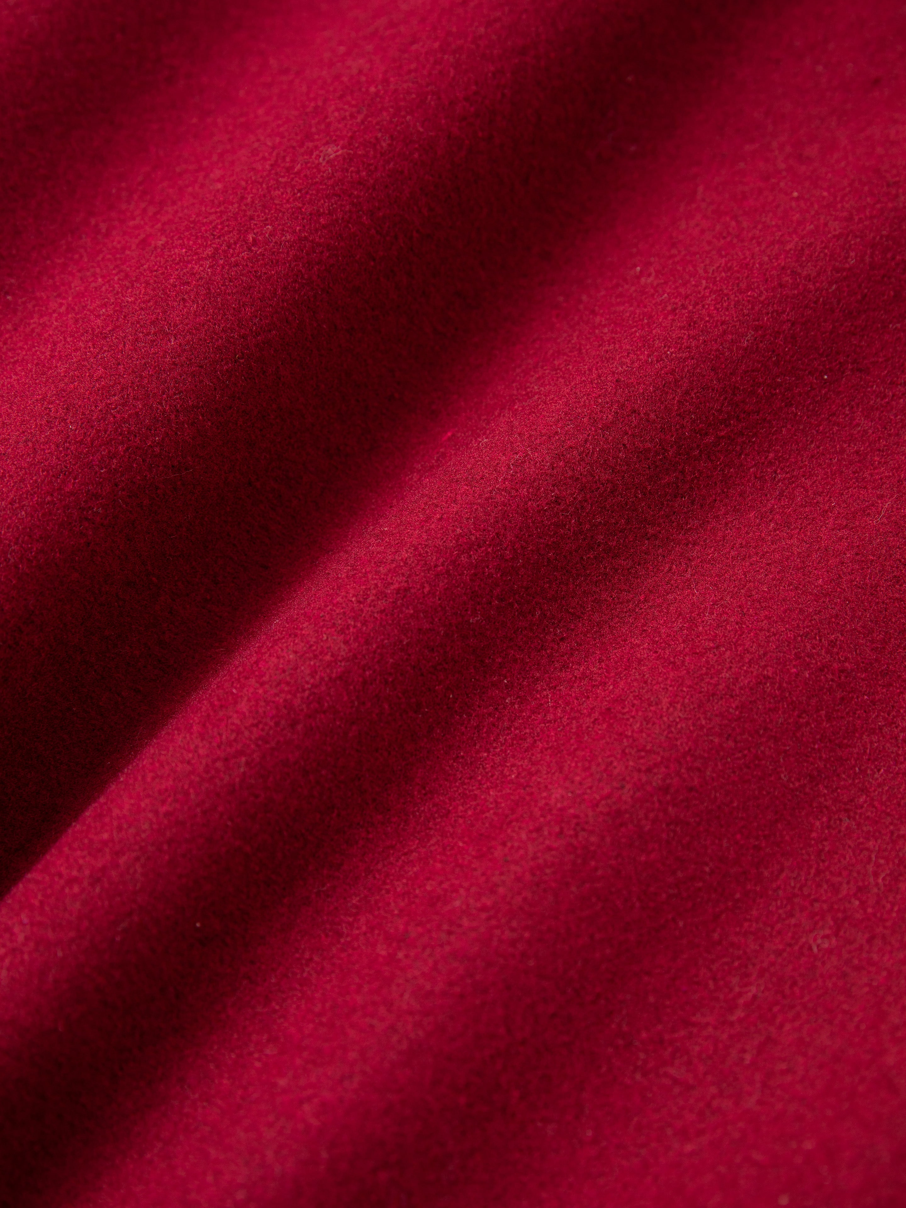 Close-up of red fabric with a soft, slightly textured surface and gently undulating folds, evoking the vintage look of the Crimson Letterman Jacket by Found.