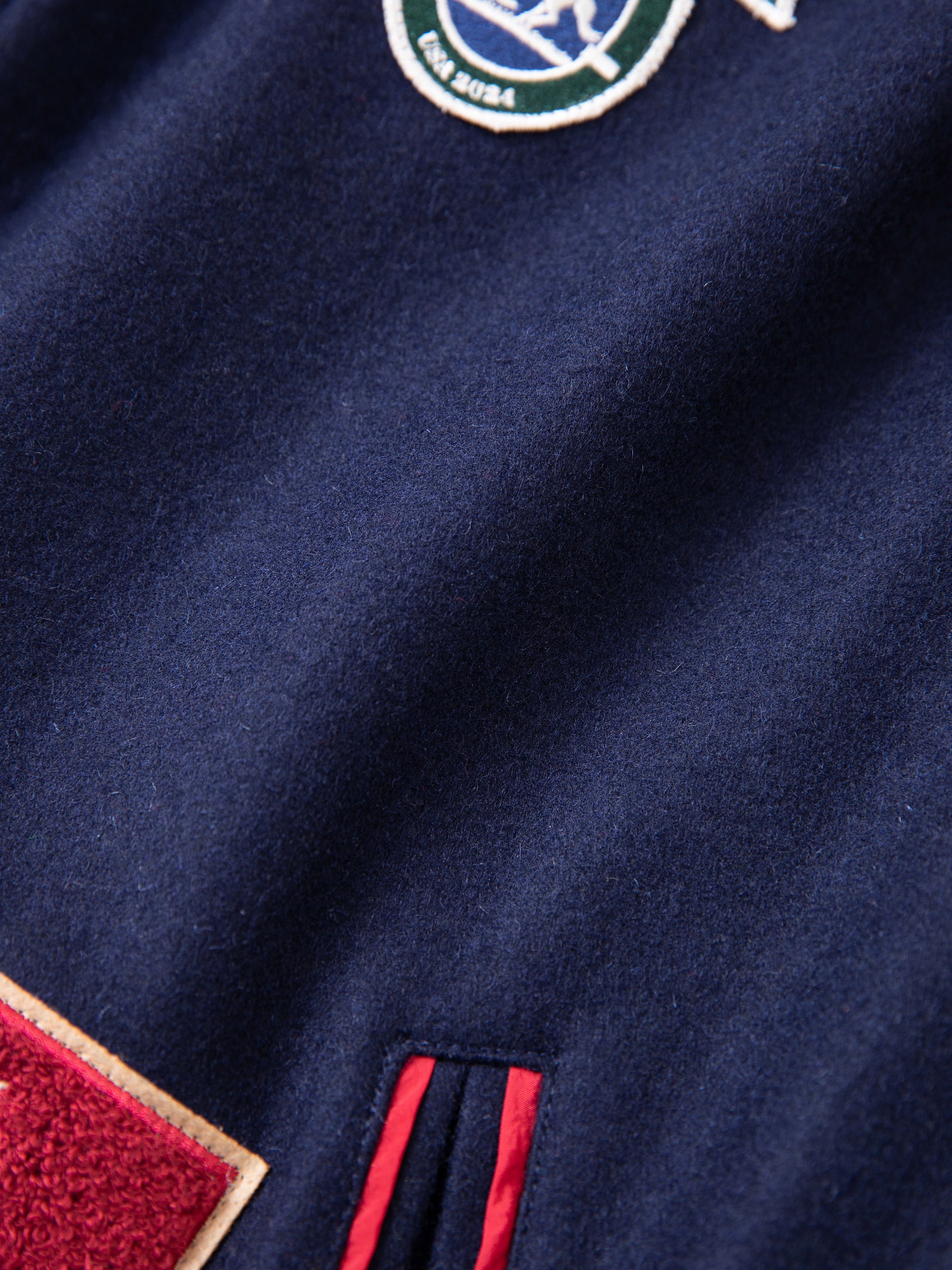 Close-up of the FOUND All Roads Varsity Jacket's navy blue fabric, showcasing a patch and red-trimmed pocket detail that give it its vintage look.