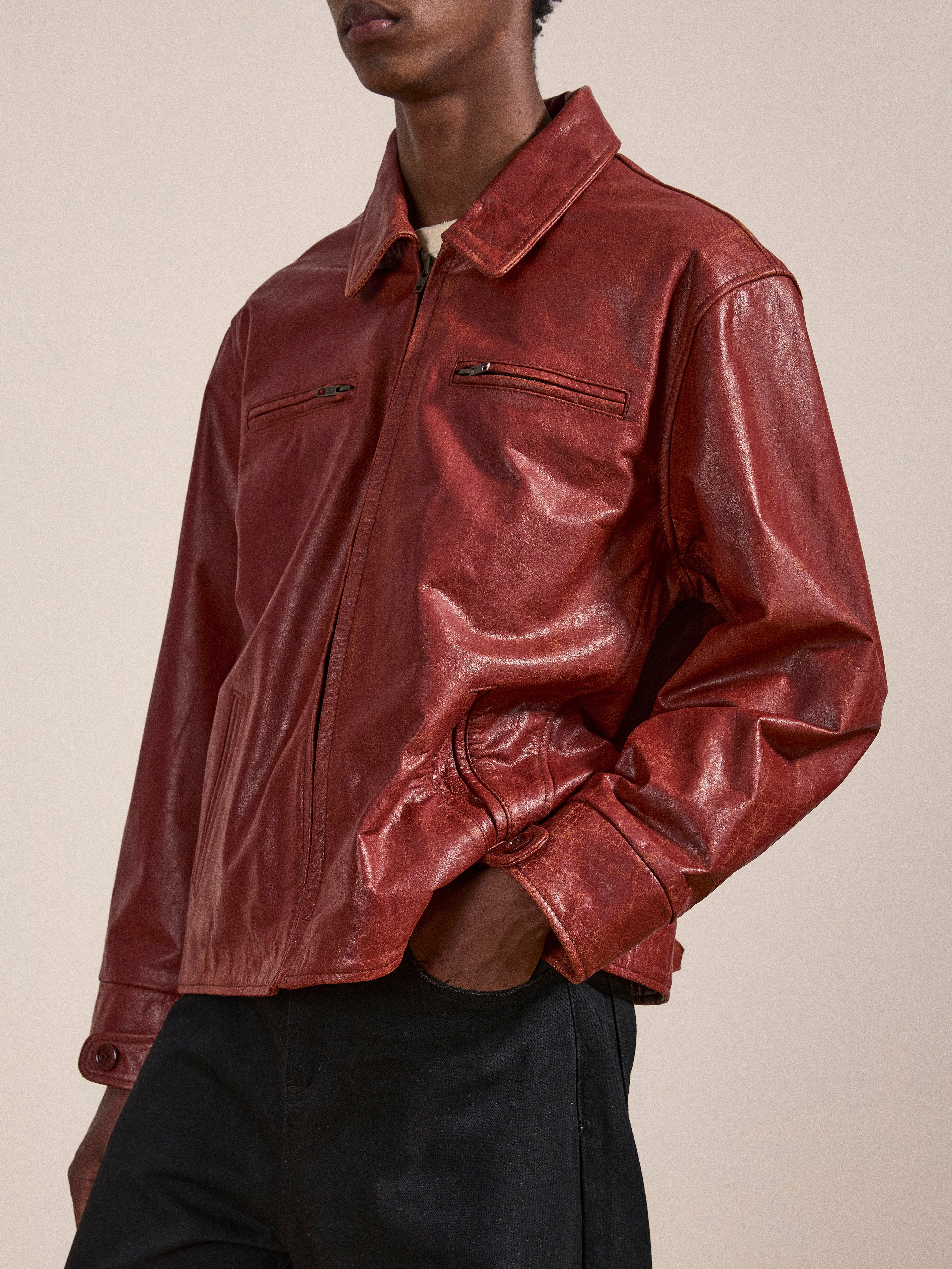 A person wearing a red leather Marlboro Sun Faded Leather Racer Jacket by FOUND with two front zipper pockets and black pants stands against a plain background.