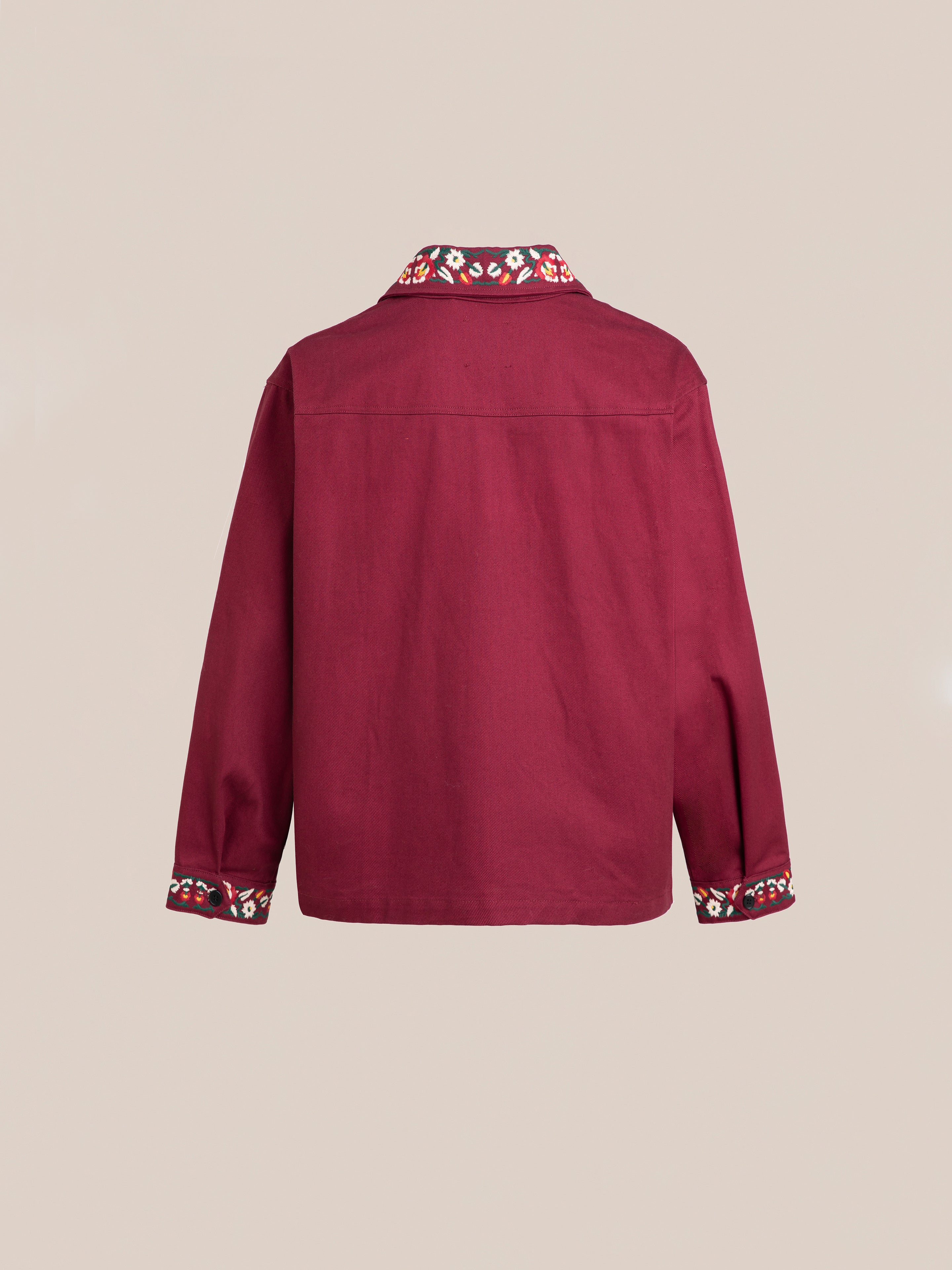 Back view of the Oxblood Horse Equine Jacket by FOUND, a long-sleeve, burgundy piece with patterned trim on the collar and cuffs reminiscent of 70's jockey uniforms, displayed against a plain beige background.