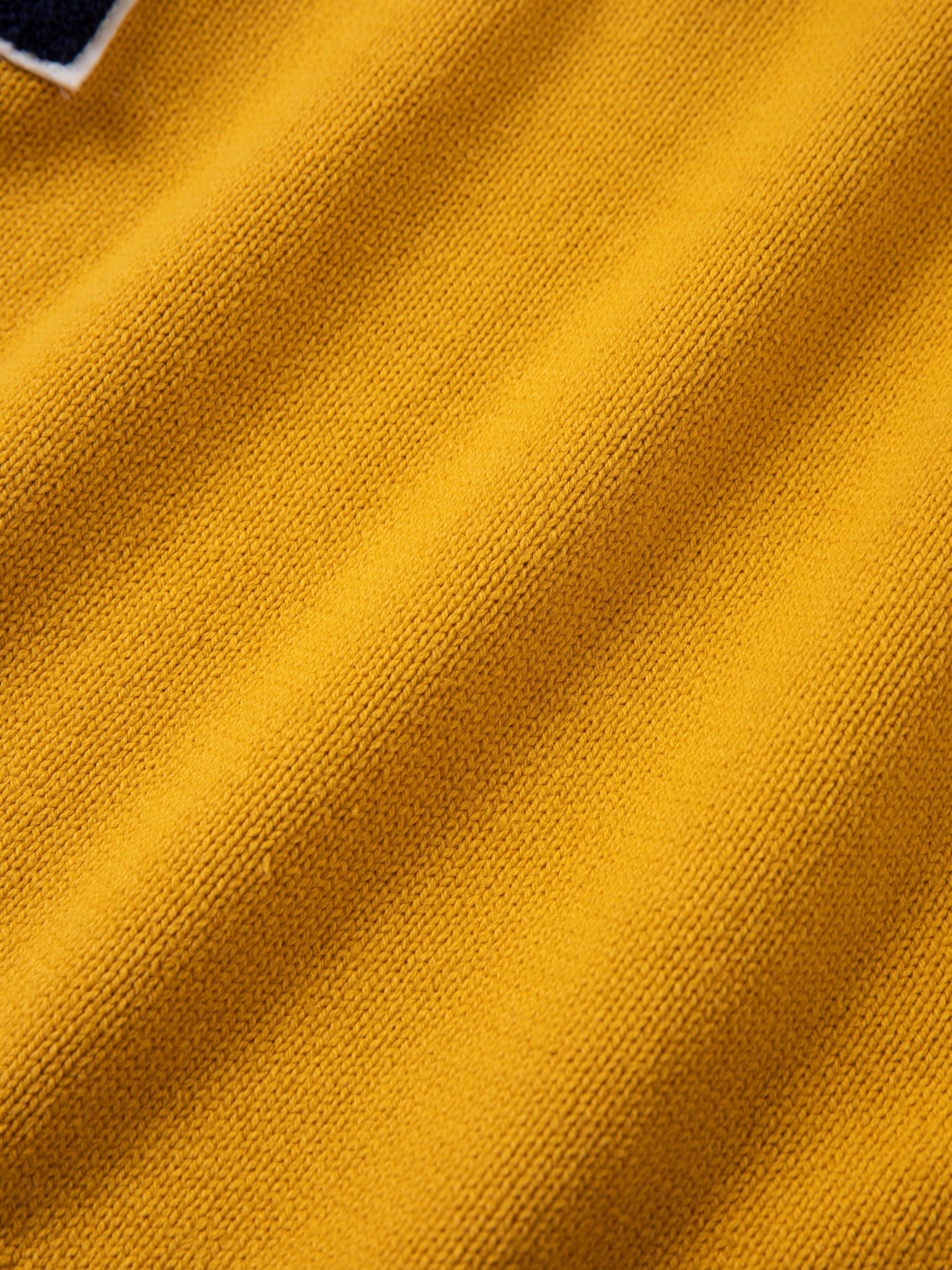 A close-up image of a textured yellow fabric with visible weave patterns, evoking the charm of a vintage look and reminiscent of the classic Arrow-Wood Varsity Knit Sweater from FOUND's Ivy League collection.