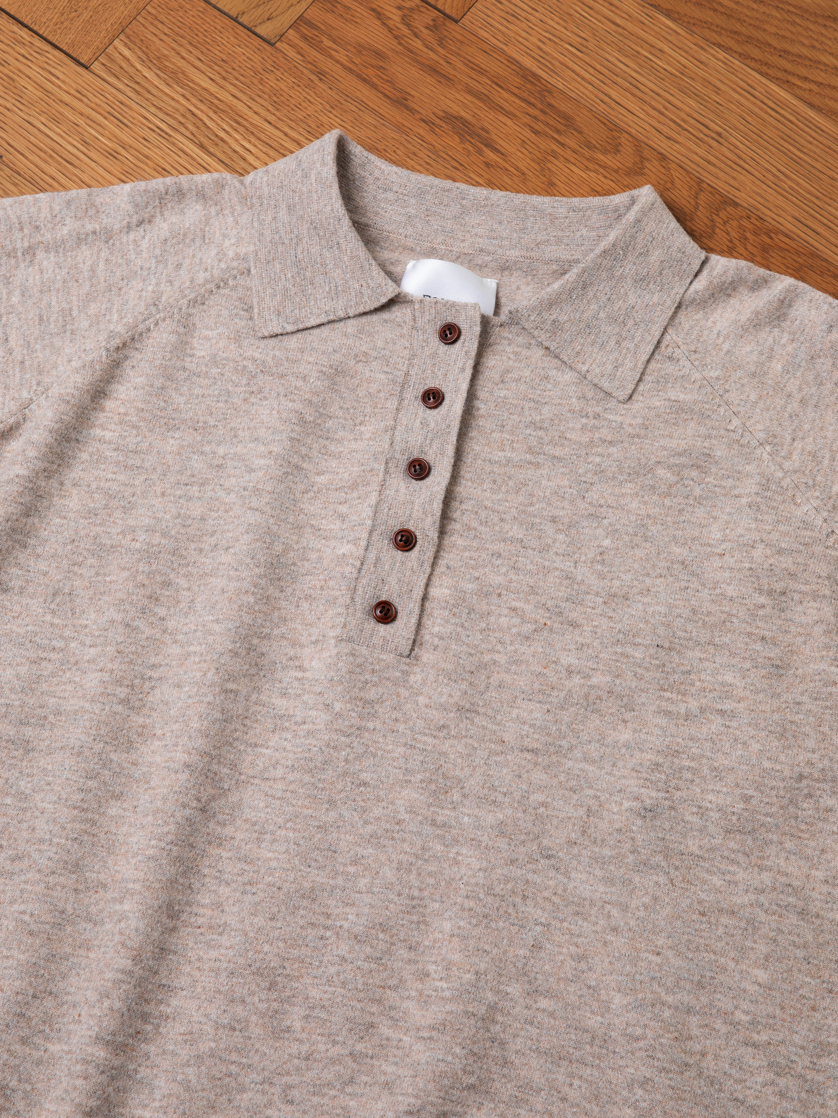 A light grey Hay Collared Knit Henley by FOUND, featuring a buttoned placket with five dark buttons, laid flat on a wooden surface.