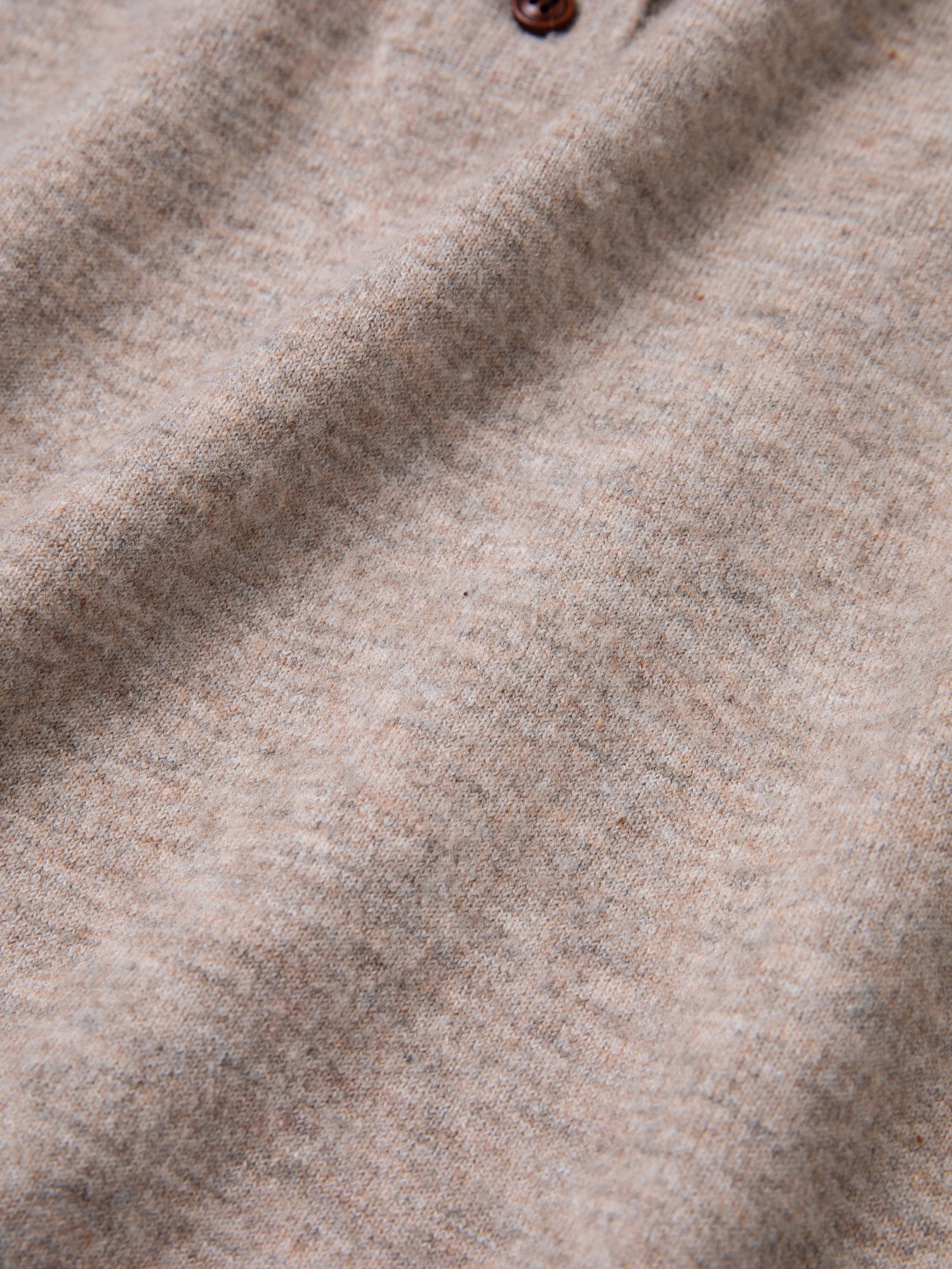 Close-up of the Hay Collared Knit Henley by FOUND, showcasing its grayish-beige wool fabric with a soft texture. Two dark brown wooden buttons are partially visible at the top of the image, adding a touch of rustic charm.