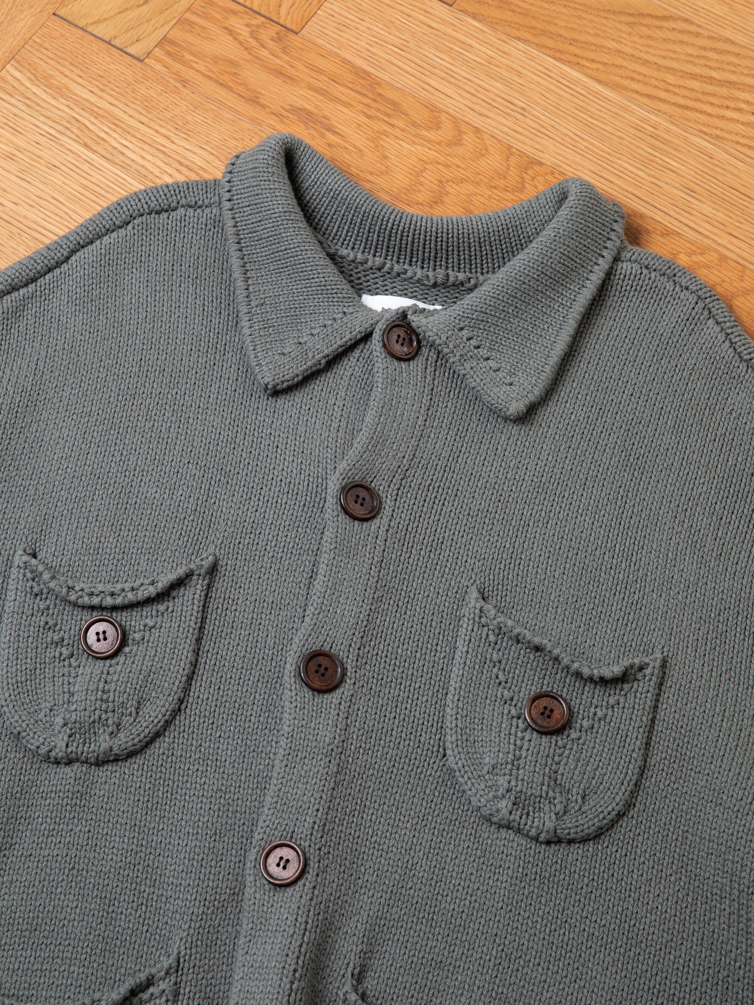 The Hunter Knit Collared Cardigan by FOUND, featuring a gray knit design with two front pockets and wooden buttons, is laid flat on a wooden floor.