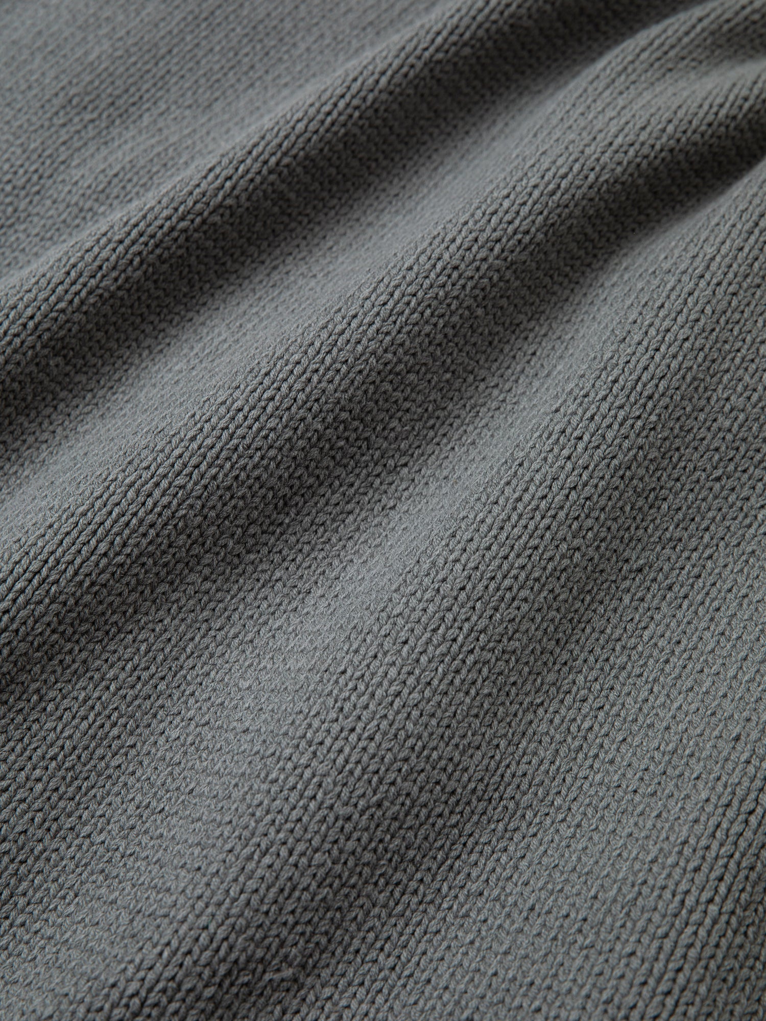 Close-up of the Hunter Knit Collared Knit Cardigan by FOUND, highlighting its grey textured fabric with a woven pattern and slight ripples, reminiscent of an oversized knit cardigan.