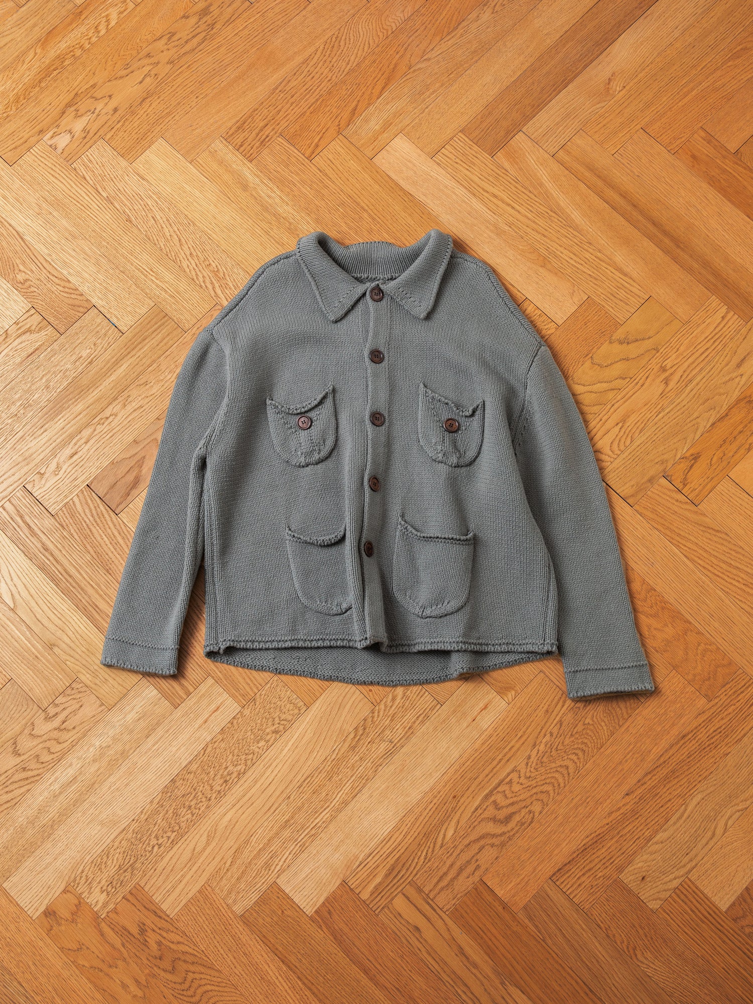 A FOUND Hunter Knit Collared Knit Cardigan in gray, adorned with wooden buttons and four front pockets—two on the chest and two at the hip—laid out flat on a wooden parquet floor.