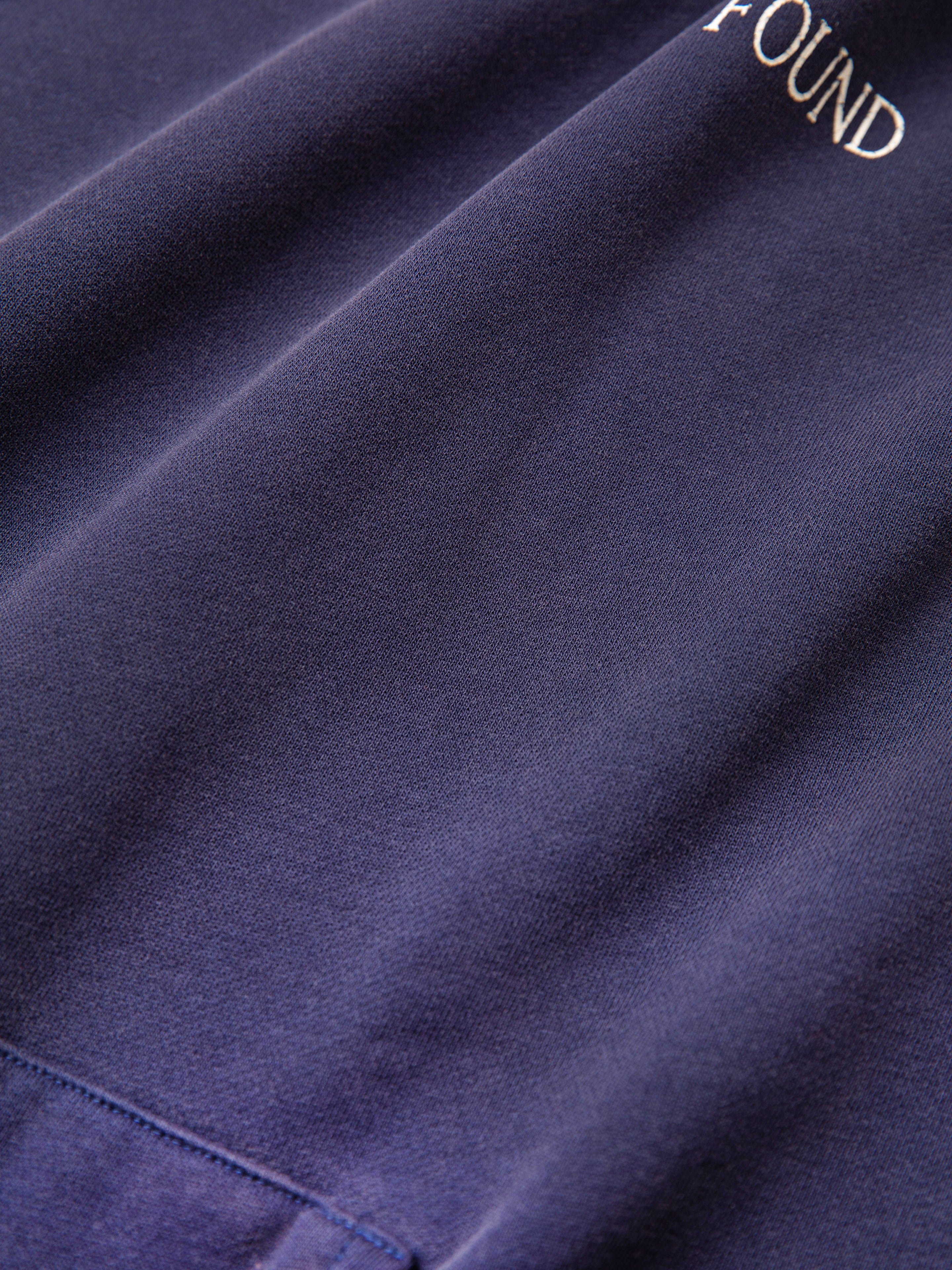 Close-up of a folded dark blue French terry cotton fabric from the Distressed Logo Hoodie by FOUND, with the brand name partially visible at the top right, evoking a vintage feel.