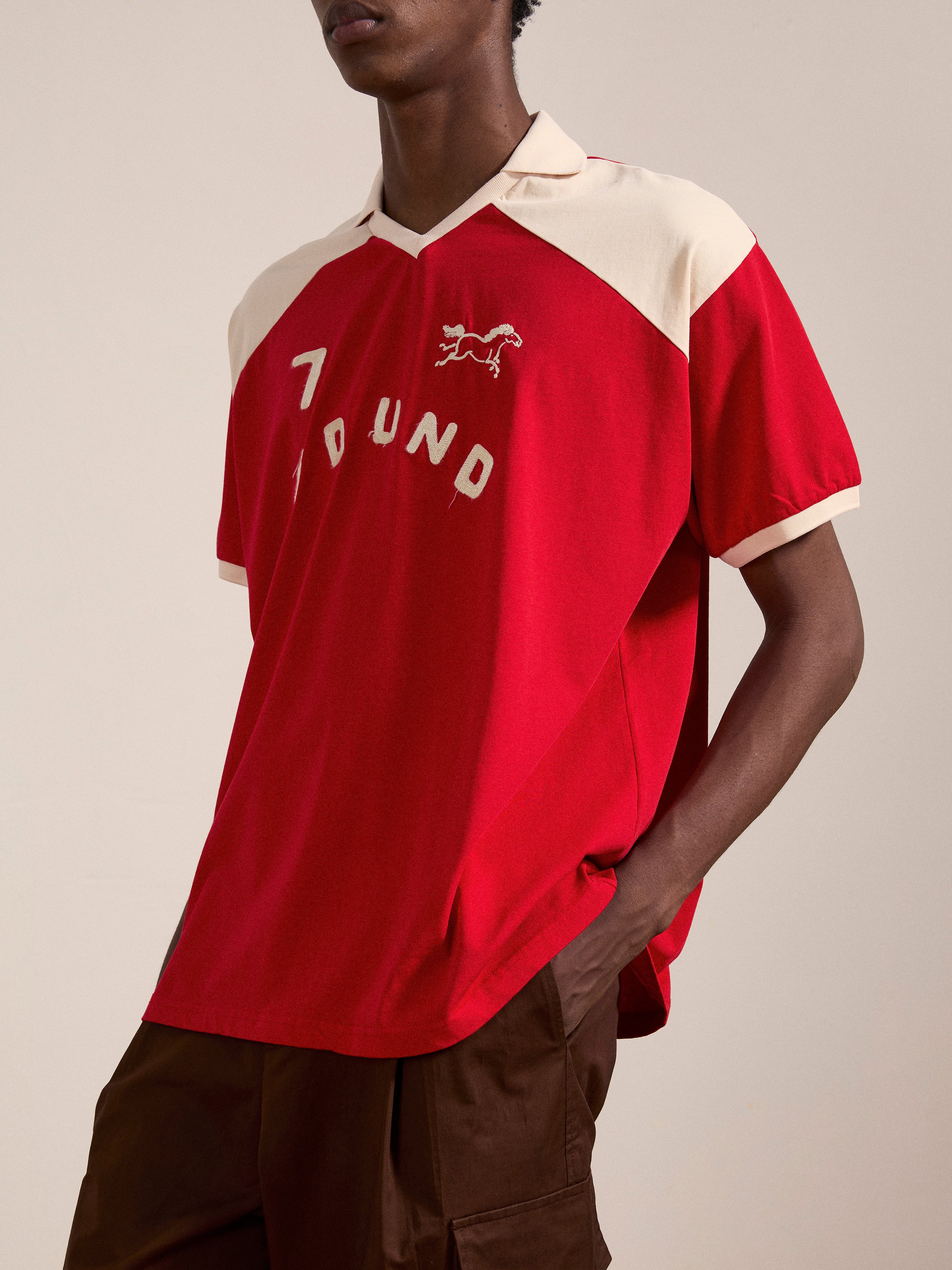 Person wearing a Goji Red Jersey from FOUND with an animal logo on the front, featuring a contrast color yoke and collar, paired with brown pants.