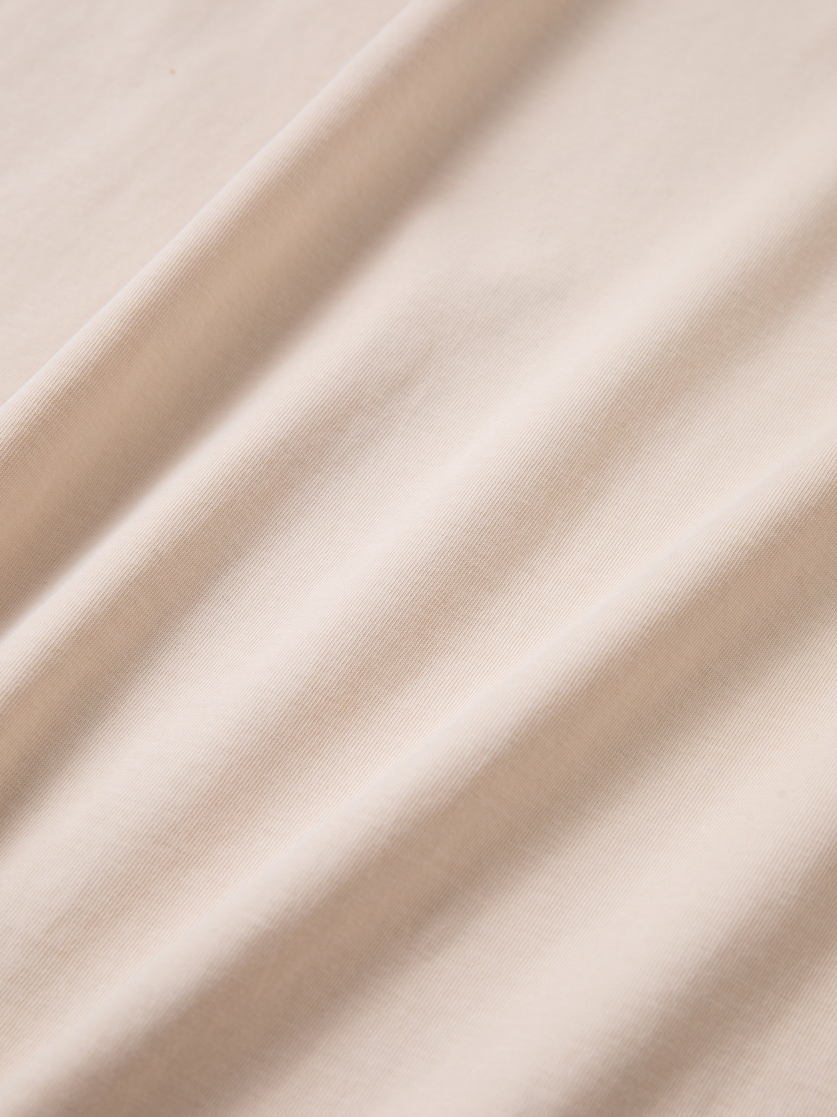 Close-up of light beige fabric with smooth texture and gentle folds, reminiscent of the classic Cascade Floral Ringer Tee by FOUND.