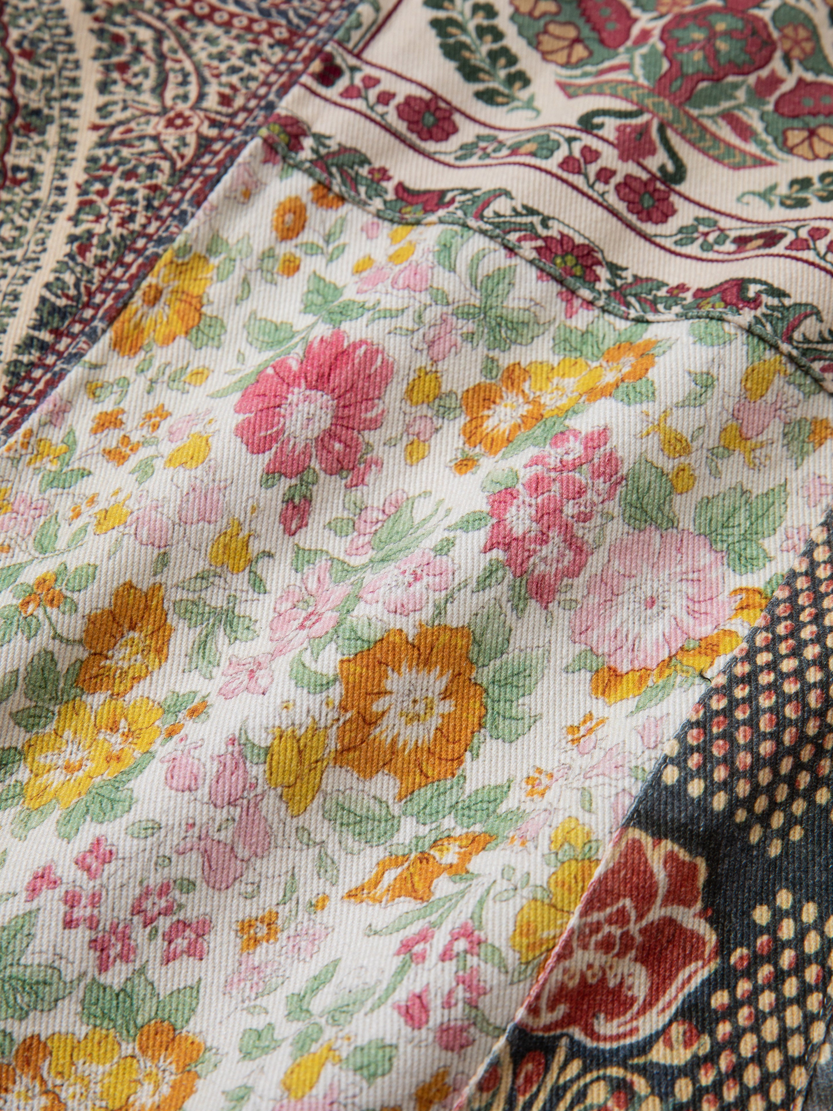 Close-up of the Tapestry Twill Jacket by FOUND, showcasing its lightweight cotton twill fabric adorned with various patterns, including pink and yellow flowers on a white background, as well as intricate South Asian geometric and floral designs in red, green, and blue. Perfect for a chic look.